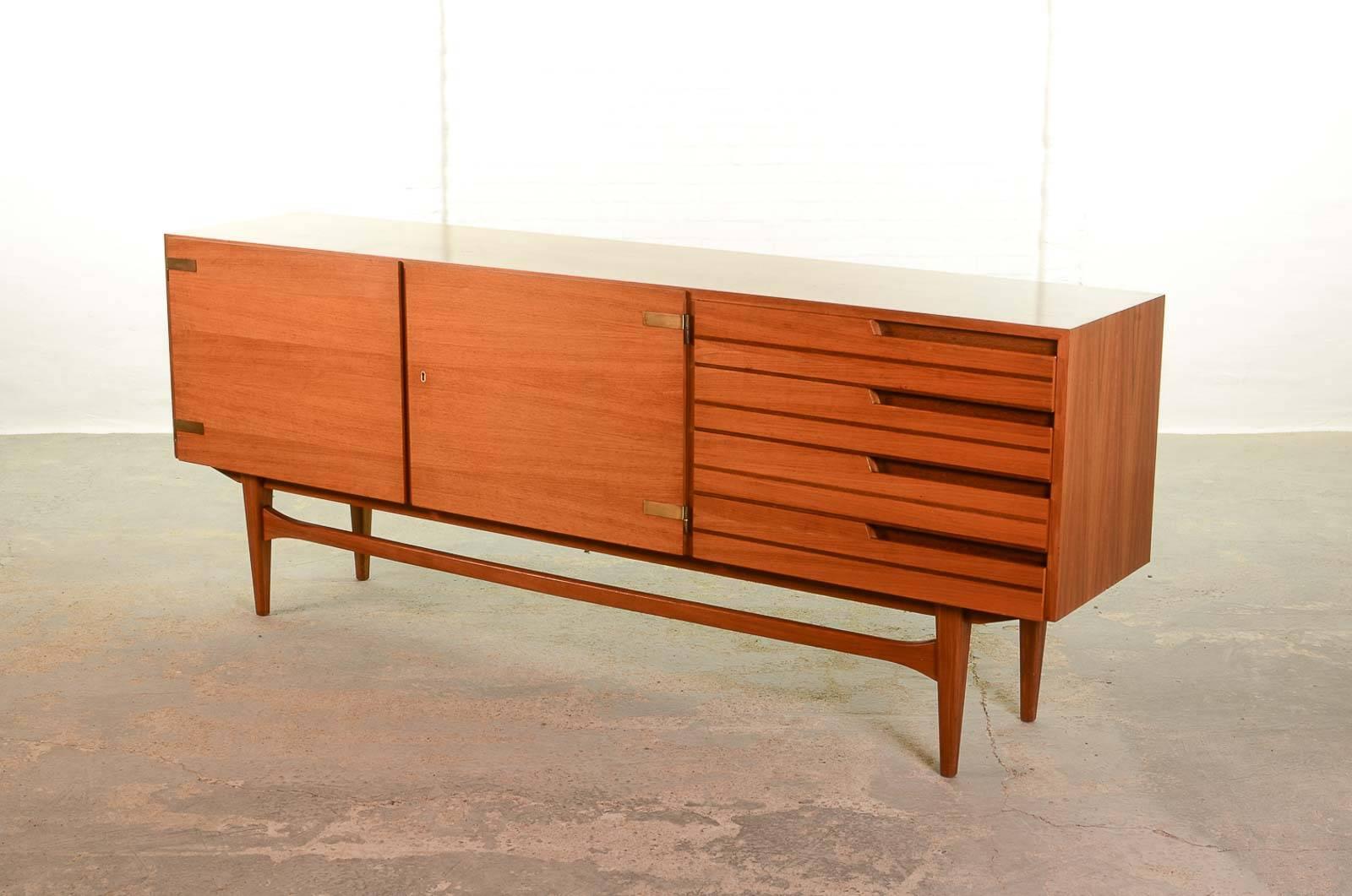 Satinwood teak sideboard/credenza decorated with elegant brass hinges. The right side of the sideboard contains four duotone wooden drawers with partly carved out strips suggesting subtle handgrips. The design shows a variety of Fine details