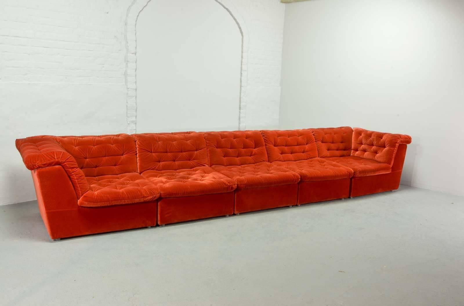 This stunning and very comfortable sofaset contains five elements and a separate lounge chair in a beautiful bright vermilion red colored velvet / velours upholstery. 
All elements are interchangeable, so there are numerous ways to put it. The set
