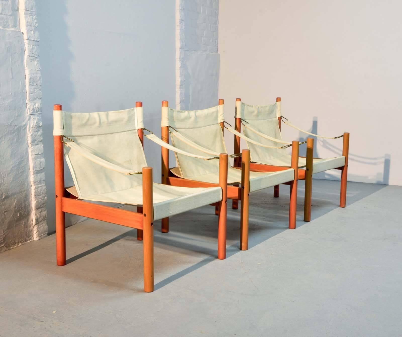 Set of three authentic midcentury armchairs with a safari style construction. This Scandinavian canvas set with solid carrot red colored wooden frames which is in style of the Danish designer Erik Worts, is produced in the 1960s. The chairs are in