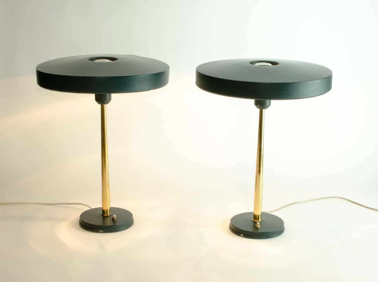 Midcentury original pair of brass table / desk lamps in dark green, designed by Louis Kalff for Philips, The Netherlands. 
This famous 'Timor 69' Dutch design features a dark green foot and an UFO shaped aluminium lampshade on a brass pedestal.