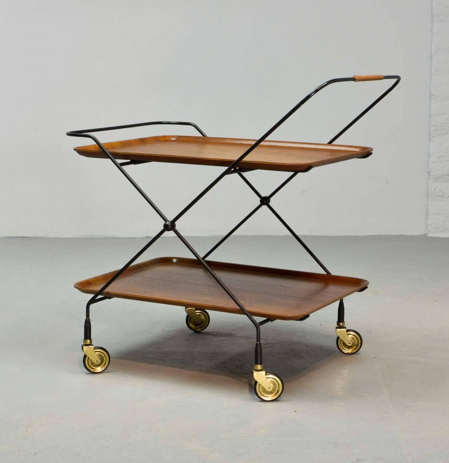 This beautiful foldable and mobile teak trolley on a minimalistic steel base, was designed by Paul Nagel, Germany in the 1950s. Nice details are the strapped leather handgrip leather and the elegant brass wheels. Fits very well in a minimalistic