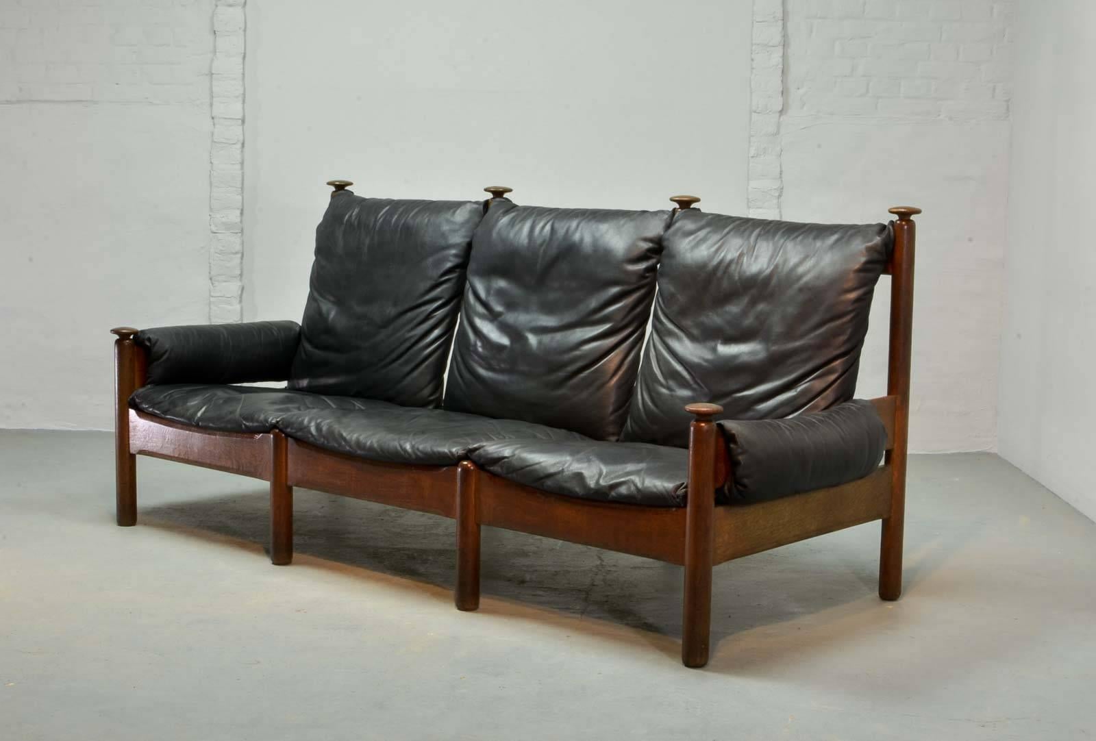 Sturdy midcentury soft black leather Scandinavian sofa produced in the 1960s in style of the Danish designer Arne Norell. The sofa features an oak wooden base with knobs and black leather upholstery which is in an overall good condition. Two lounge