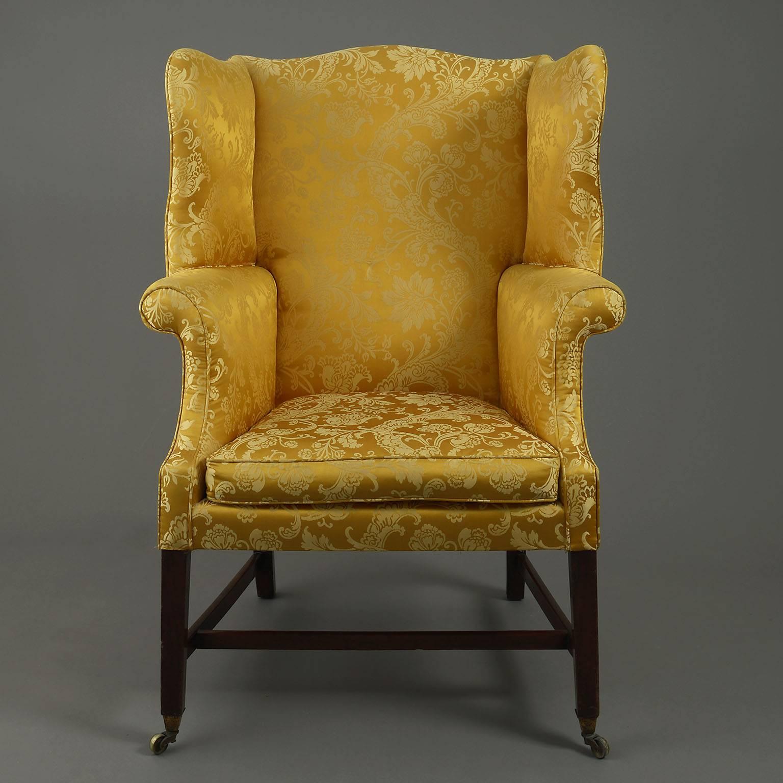 The silk-damask upholstered frame of particularly handsome and elegant proportions, with deep wings and scrolling arms. The loose-cushioned seat raised on tapering mahogany legs joined by stretchers and terminating in brass castors.
 
