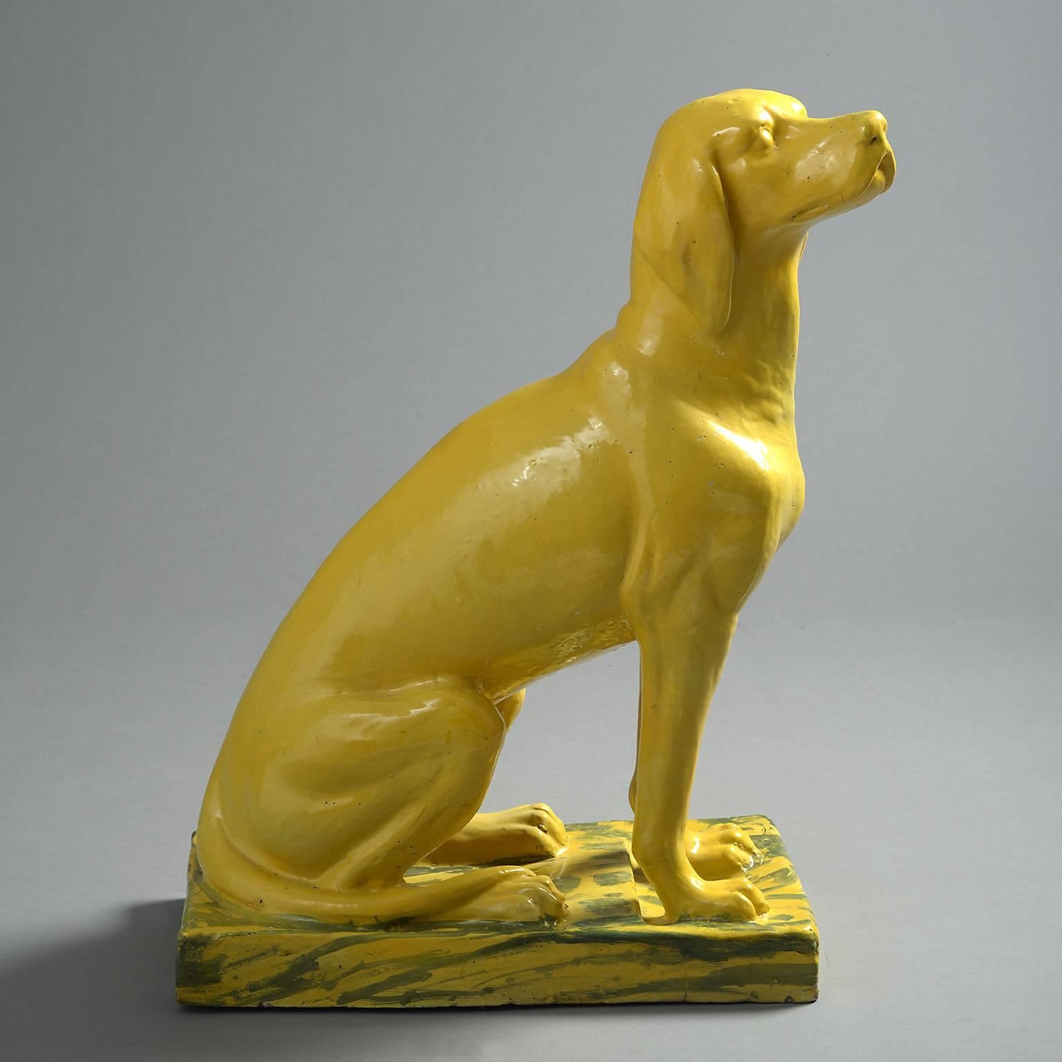 The vivid yellow glazed canine modelled in a majestic, seated position on a yellow and blue marbled base.

          