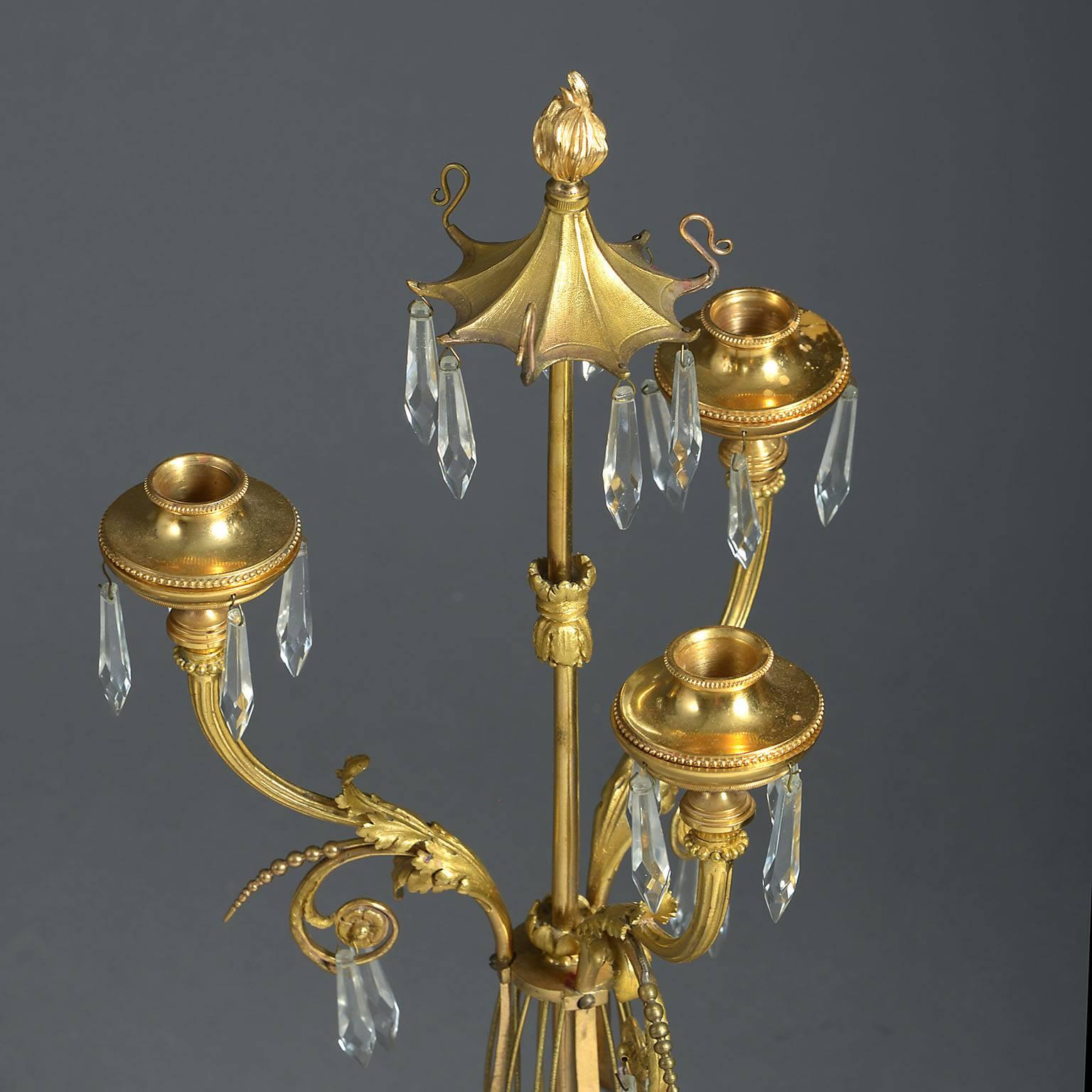 Each with three drop-hung scrolling gilt-metal candle arms with central pagoda hung with crystal drops on a gilt-metal central stem of stylised lyre form standing on ormolu-mounted turned Carrara and bleu turquin marble bases.


