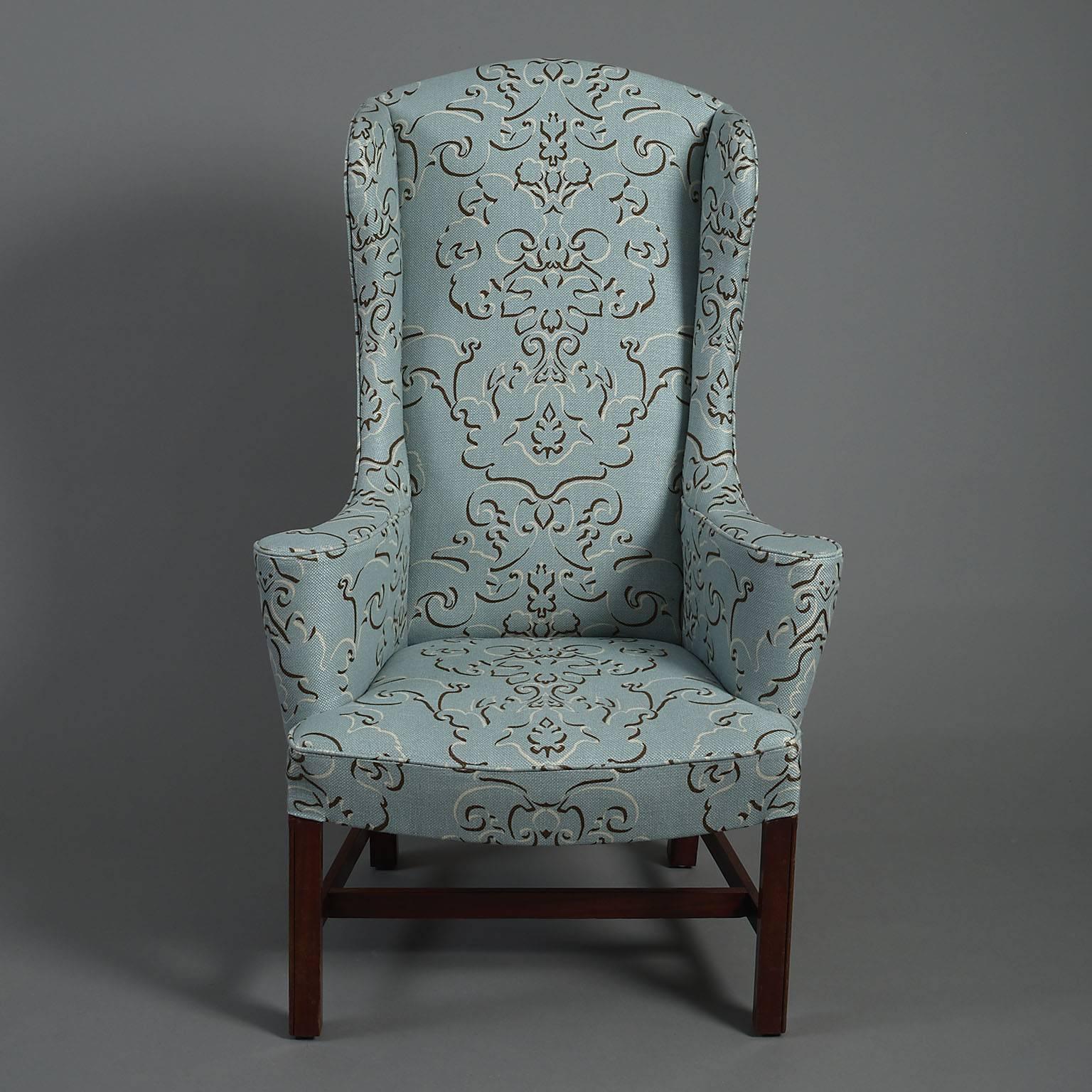 High wingback armchair in George III style.
The high arched-back with outswept arms above a dished seat raised on canted mahogany legs joined by 
