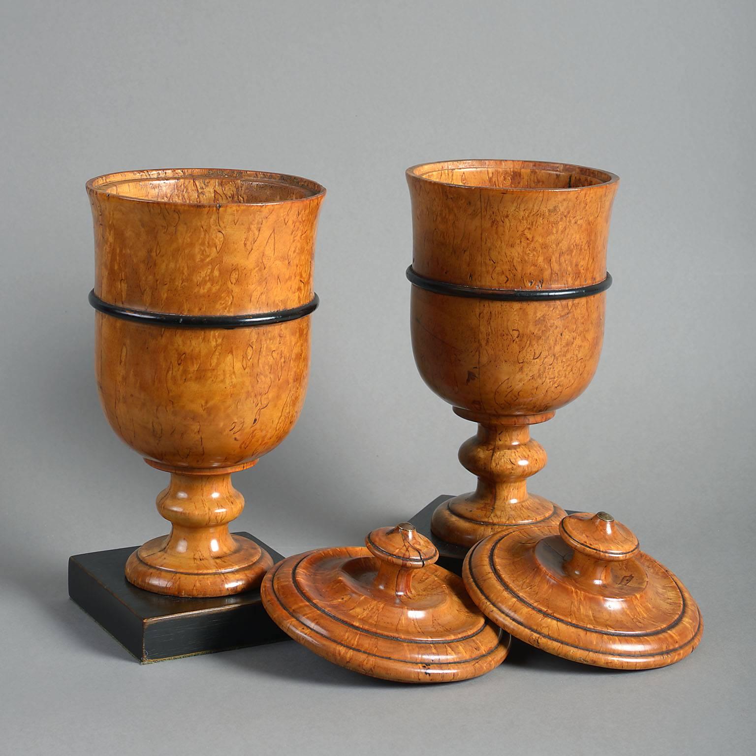 The highly figured Masur Birch lathe-turned in the form of goblets with knopped stems with ebonized bands below removable covers and standing on ebonized block bases.

Masur or Karelian Birch was used extensively in Biedermeier furniture because