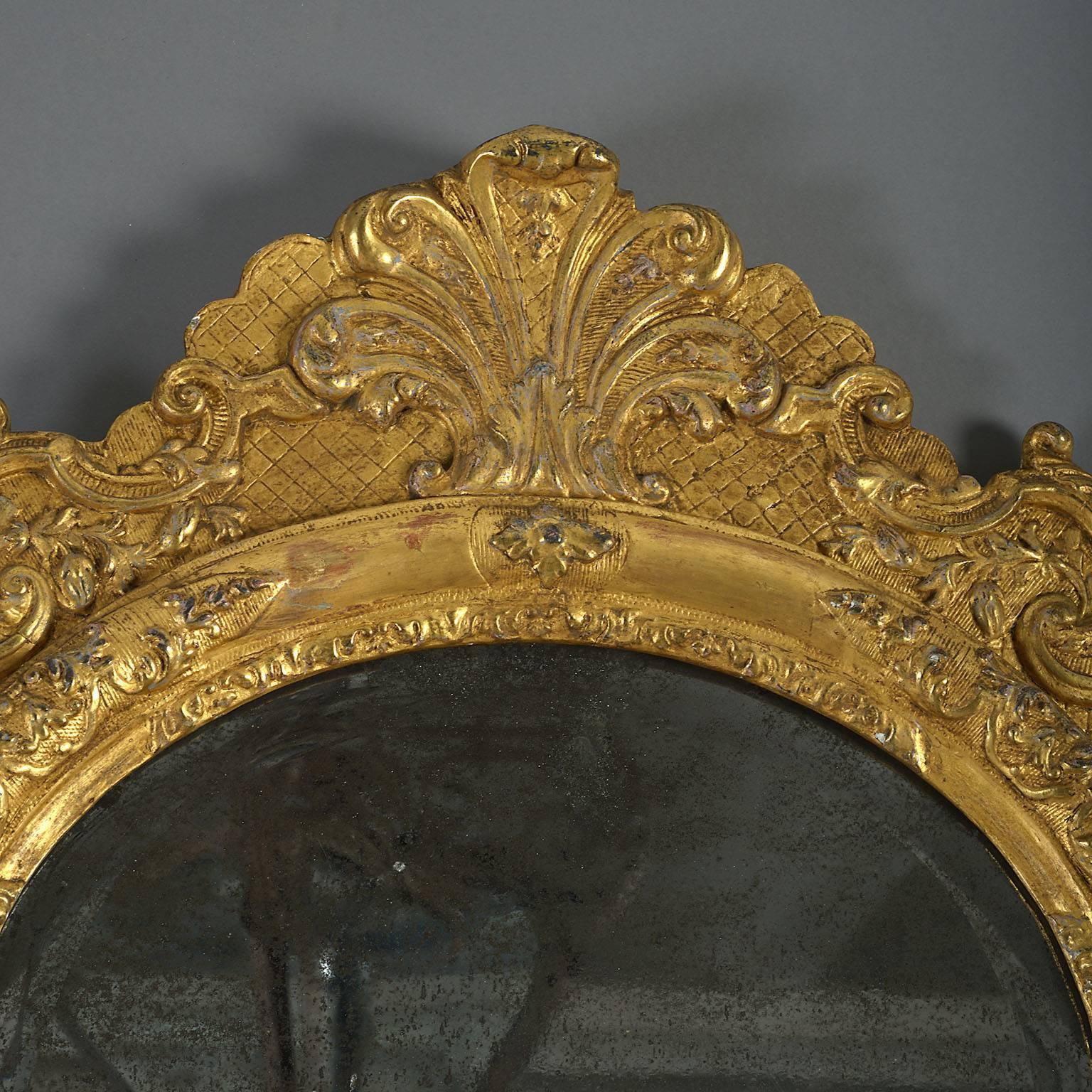 The original arched, divided mirror plate with softly bevelled edges contained within a moulded frame carved with panels of strapwork, stylised foliage and scrollwork and with a lambrequin cresting. This is an exceedingly rare and early