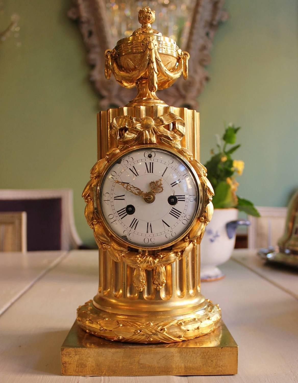 An important and elegant clock made circa 1770-1775 of very high quality. The circular gilt bronze bezel surrounded by a ribbon-tied laurel wreath mounted upon a fluted column, surmounted by a gilt bronze covered vase , ring handles and laurel
