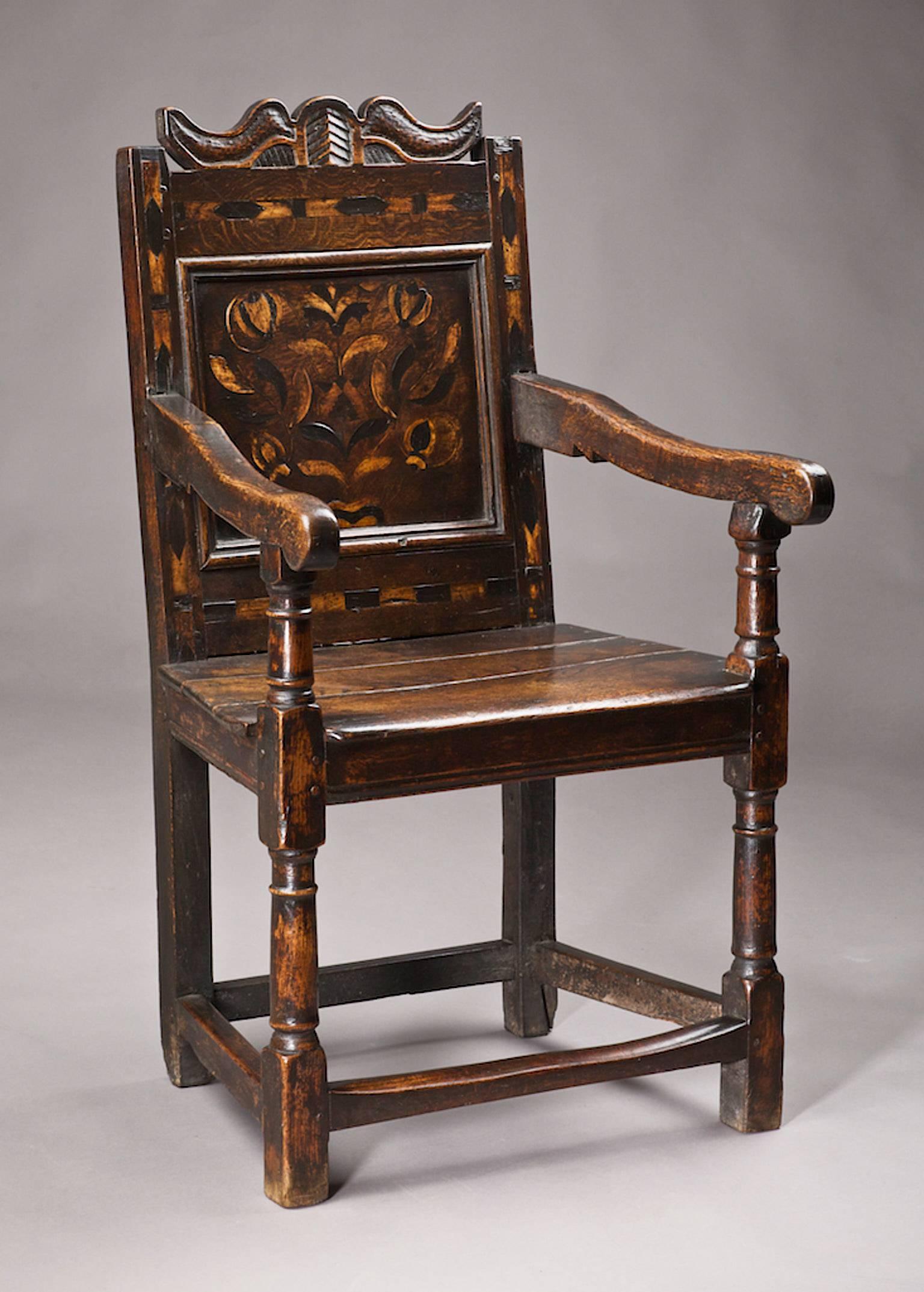 Mid-17th century Oak and Inlaid armchair, English, Gloucestershire, circa 1640-1660

The unusual scroll shaped and diaper carved cresting centred upon a palmette above bold chevron inlaid rails, with floral contrasting inlaid back panel, chevron