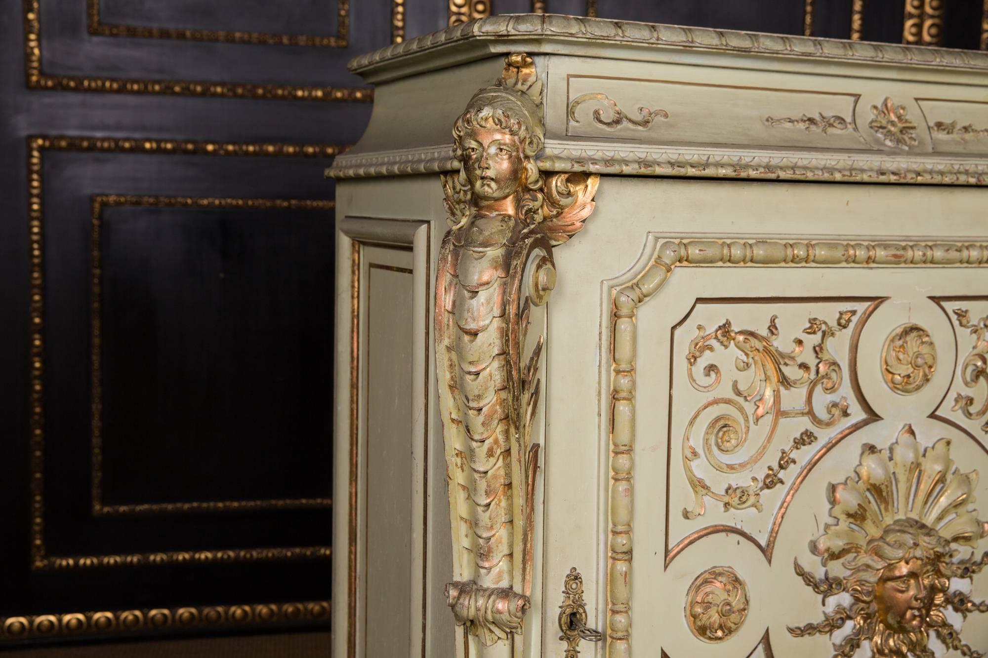 High-right, one-door corpus. In the articulated front is a wide door, carved in gold, flanked by sculptural carved female heads on a curved frame. Slightly protruding profiled frame. The chest of drawers is of exceptionally good