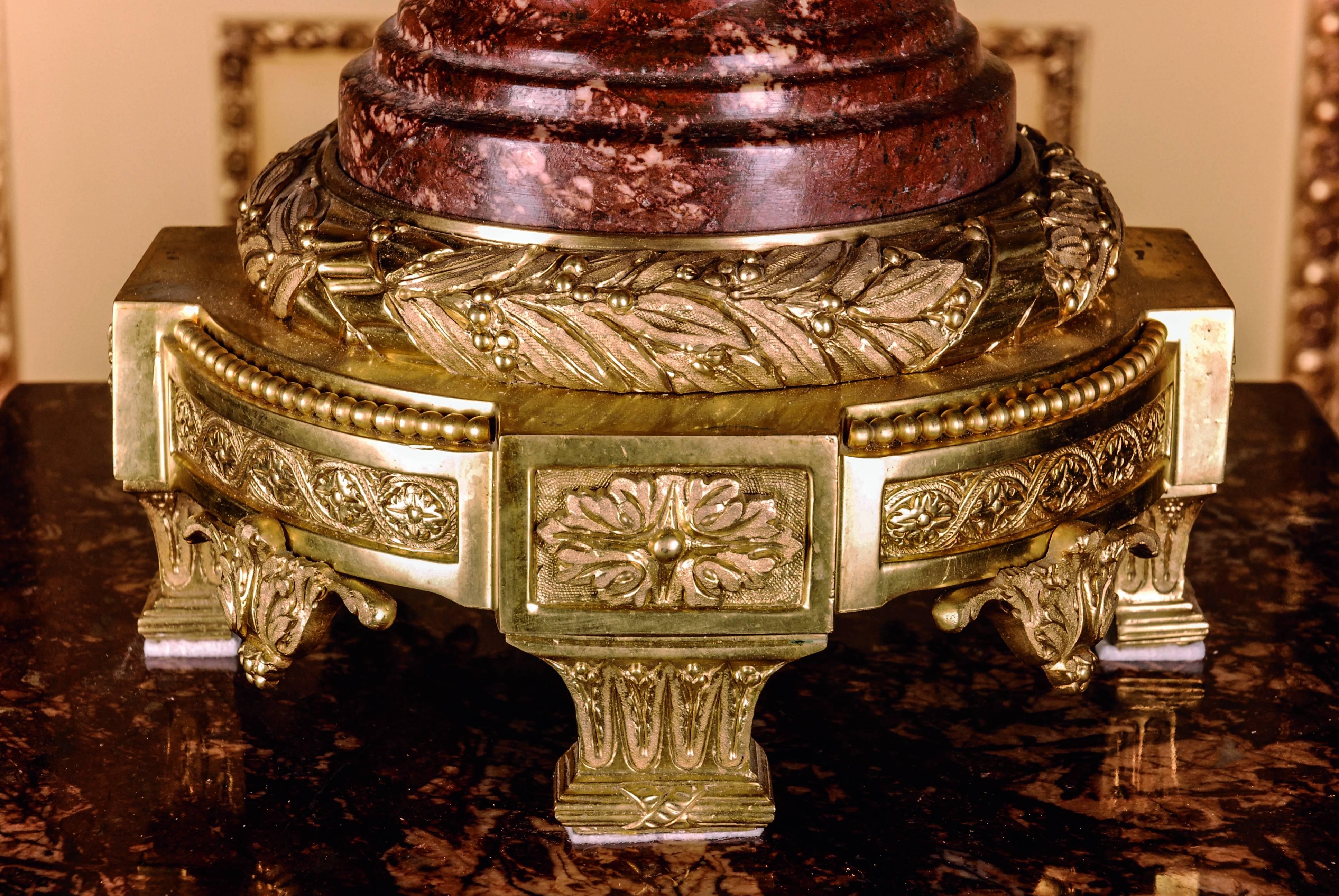 Bordeaux red marble with gray-white grain. Ovoider body with broad, ornamental and perforated hoop, decorated with chiselled Classicistic baskets, handles on both sides on high-rooted round foot, curly ascending lid crown. The chased bronze is