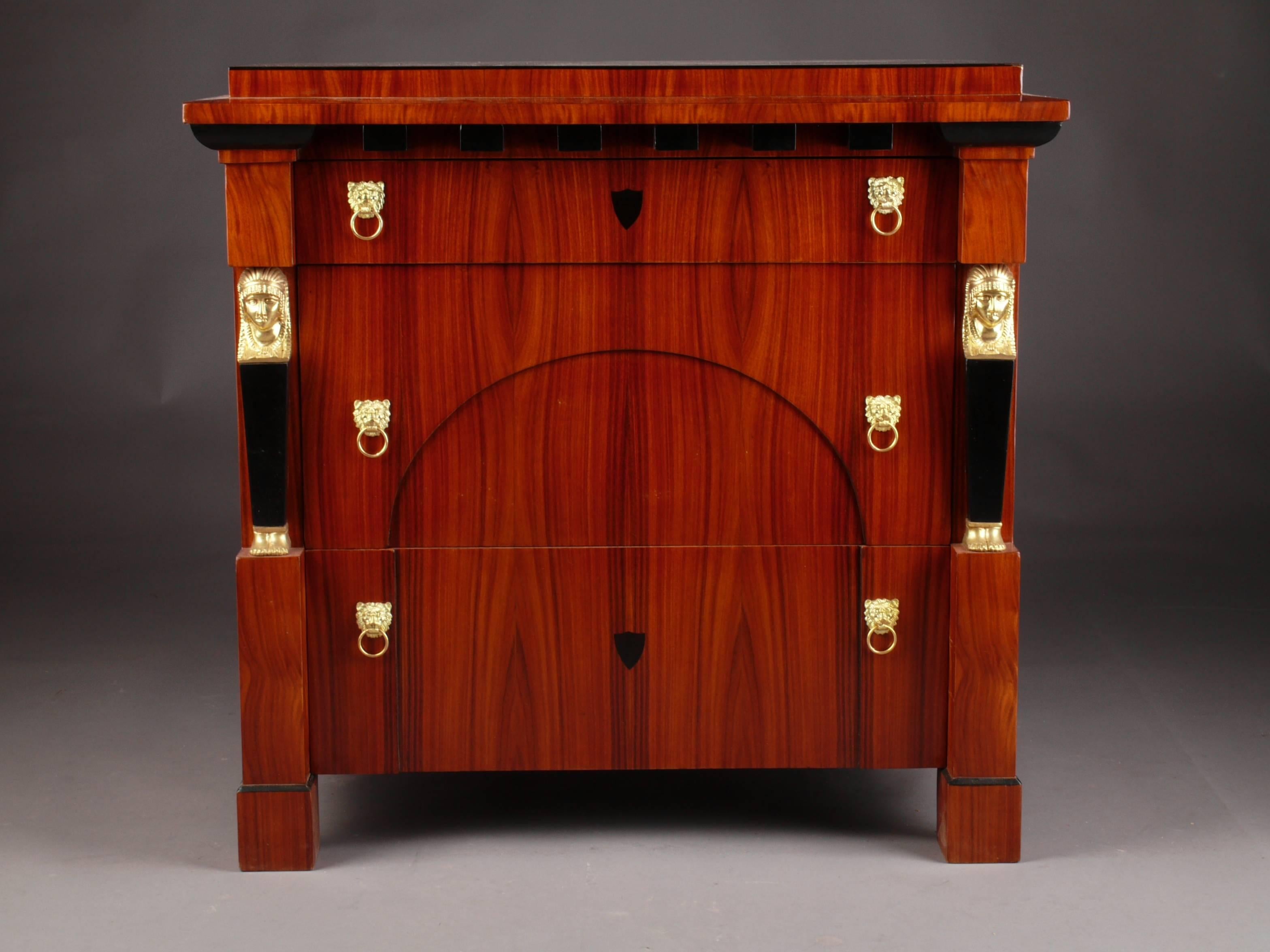 Palisander on solid conifers. Straight body on four block feet. Architecturally structured front of three drawers of different sizes, below segment-shaped filling, flanked by adjusted caryatids. Slightly protruding, profile-framed cover plate.