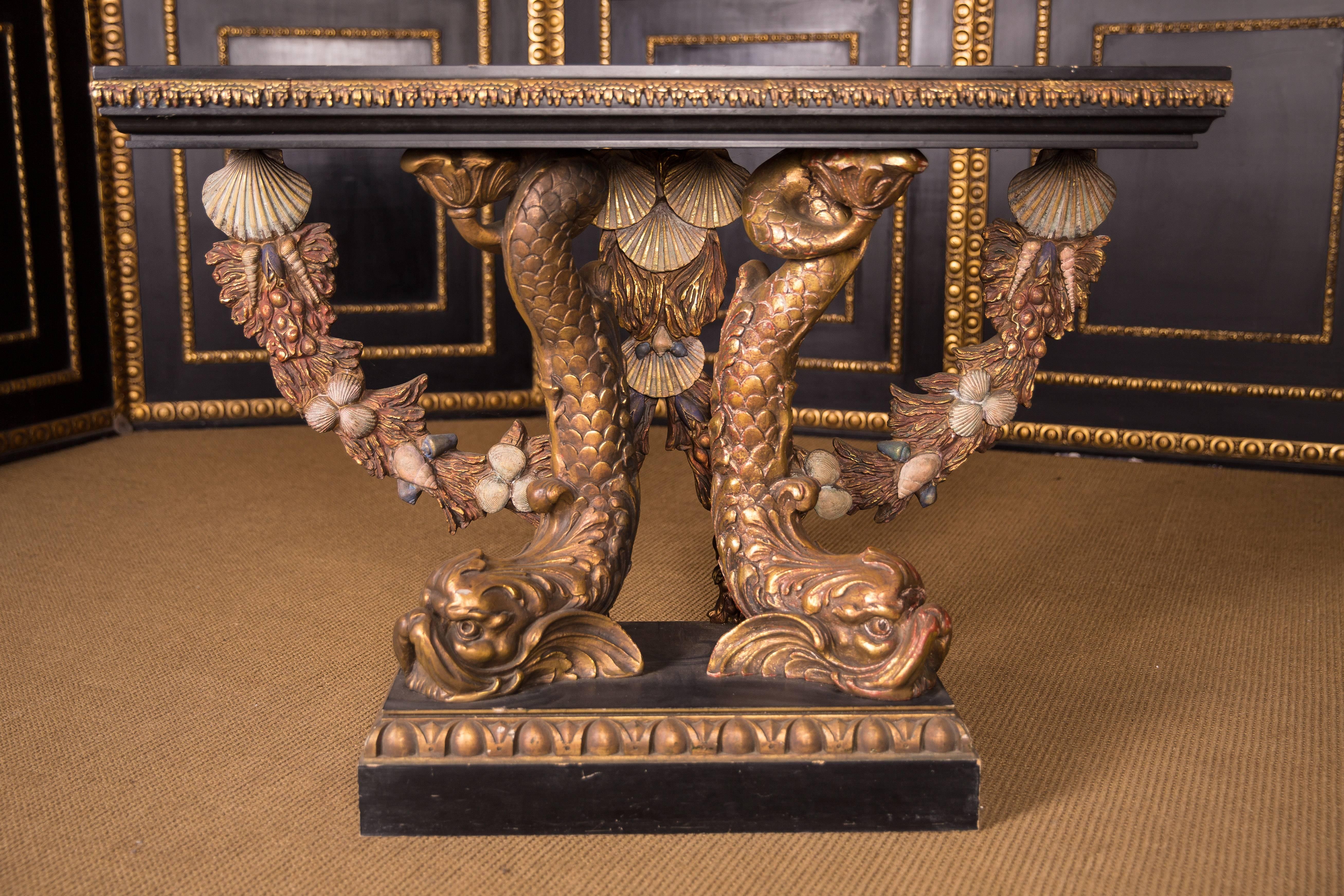 Massive, ebonized beech. A neoclassical console with two monumental, fully-plastic, hand-carved dolphins made of solid beech. Scales colored, heads and fins are antique gold. Stepped base plate, decorated with gilded decorative moldings.