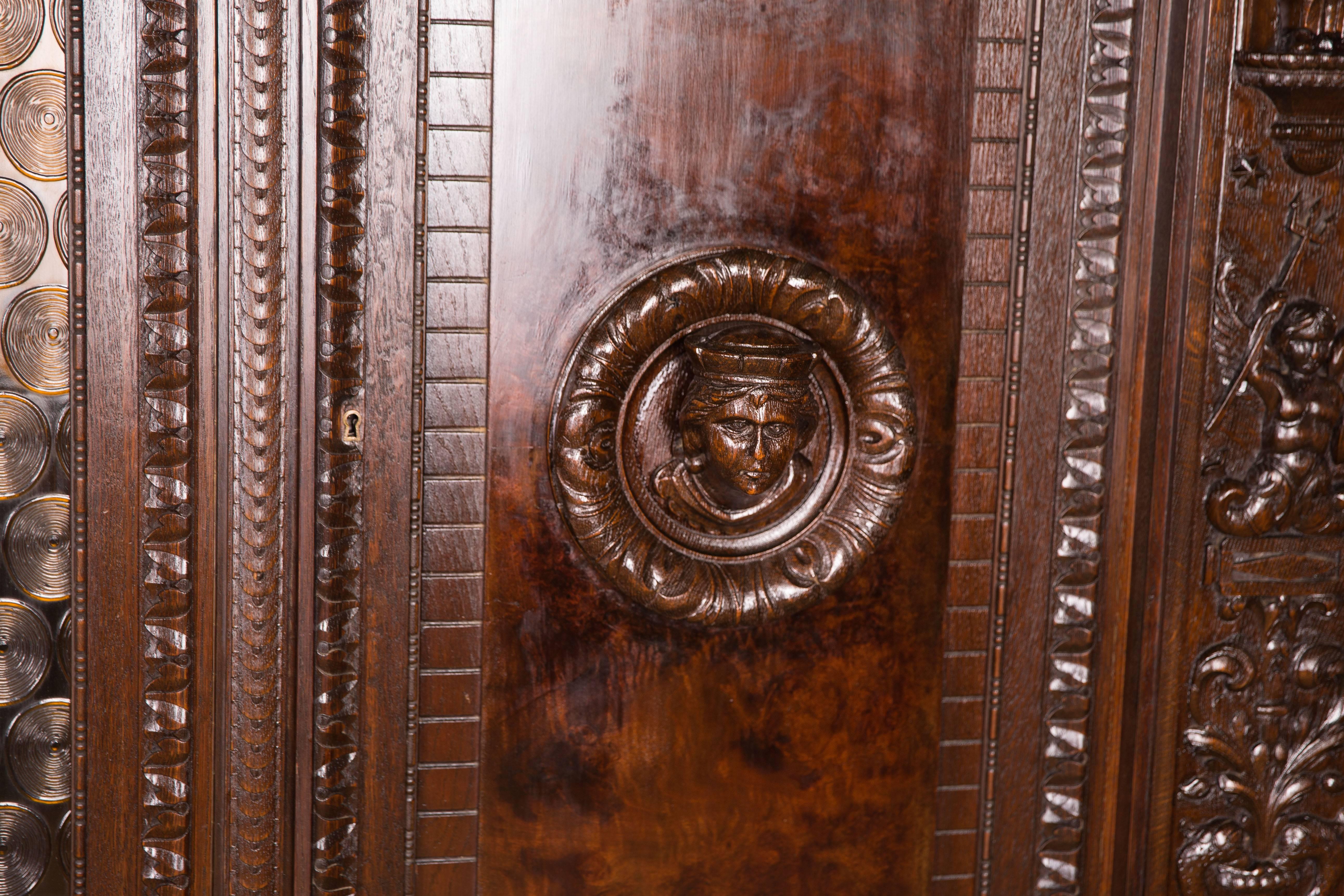 Walnut root on solid wood. Profile-framed frame base on printed pawprints. High-right, architecturally articulated body. Two doors, two glass doors in the middle. On the sides of the corpus are carvings and carved figures. Highly profiled