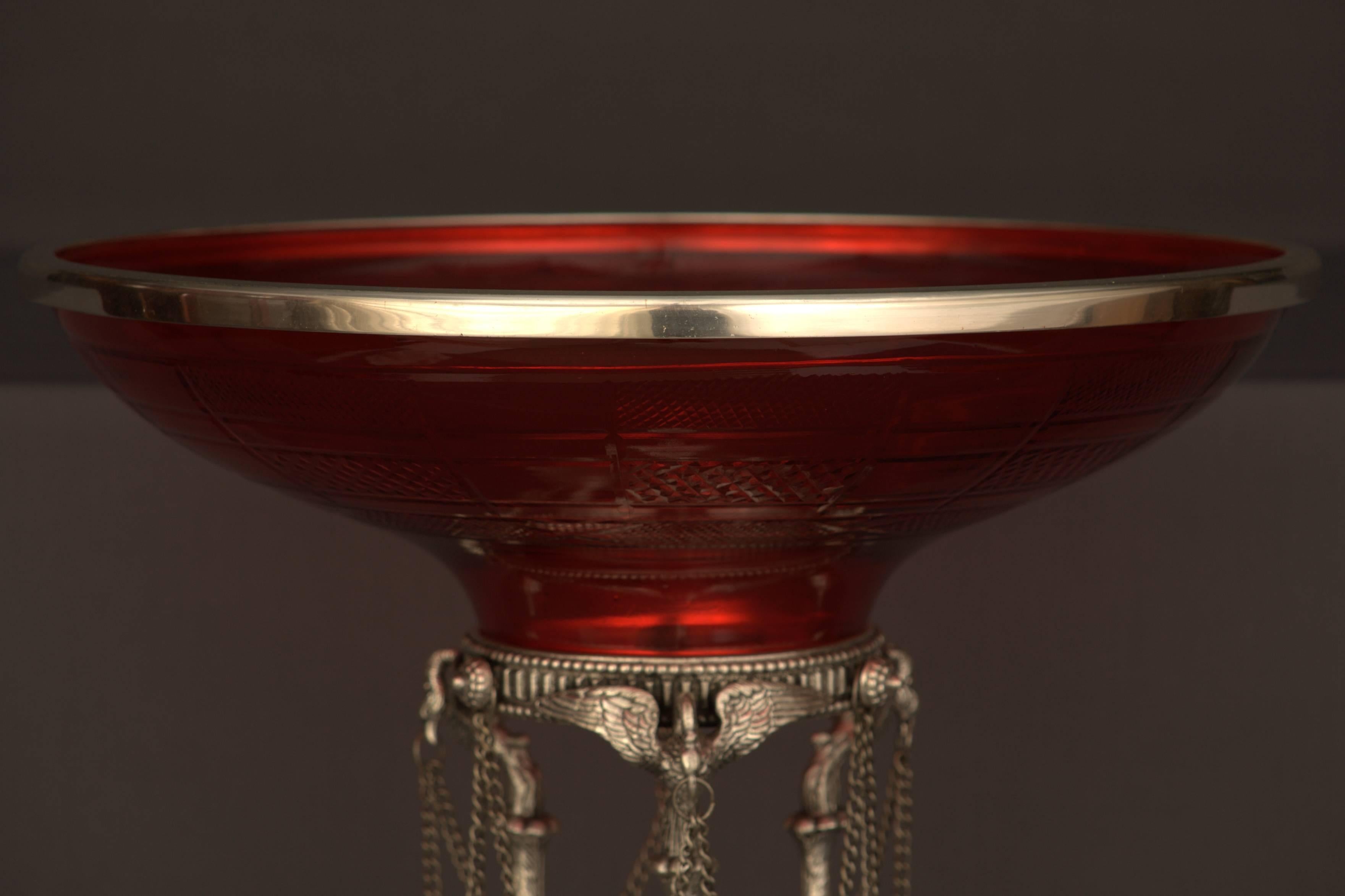 Bronze, engraved and silvered. Three column shafts with full-plastic swans.
Ruby-red glass with cut decoration. Measures: Diameter 34 cm, height: 35 cm.