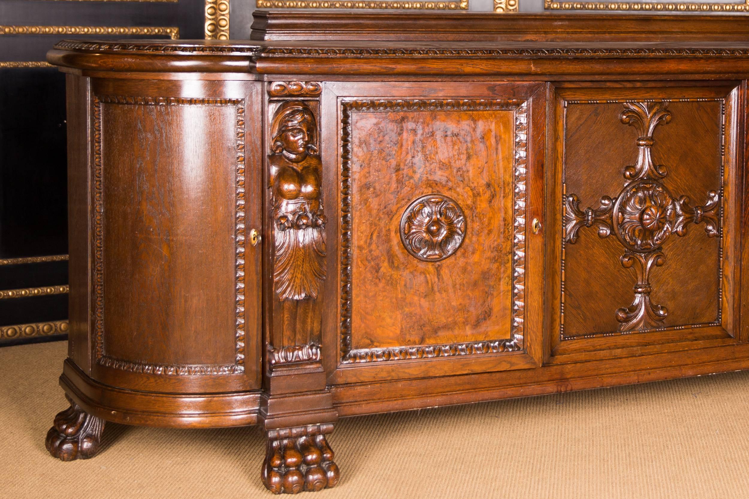 Solid oak with walnut grain. Profile framed base on pawprints. Rectangular, architecturally articulated body. Five carved doors, flanked by carved figures. Highly profiled cornice with top.