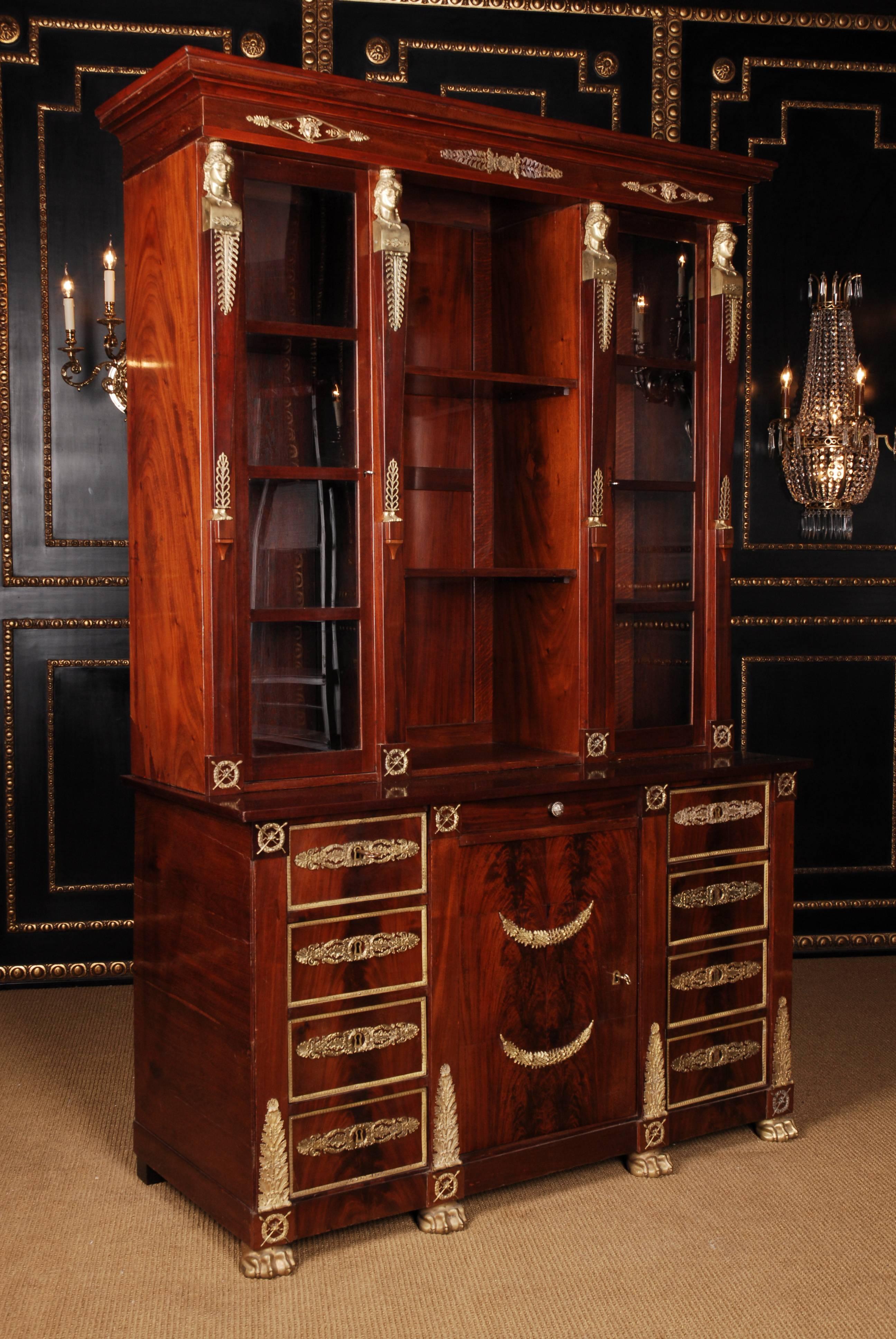Cuba mahogany on solid oakwood. Partially fire-gilded bronze fittings. Foundation base on bronze paw feet. High-rise, architecturally designed corpus. In the front center door flanked by drawers and glare door. Slightly protruding top plate,
