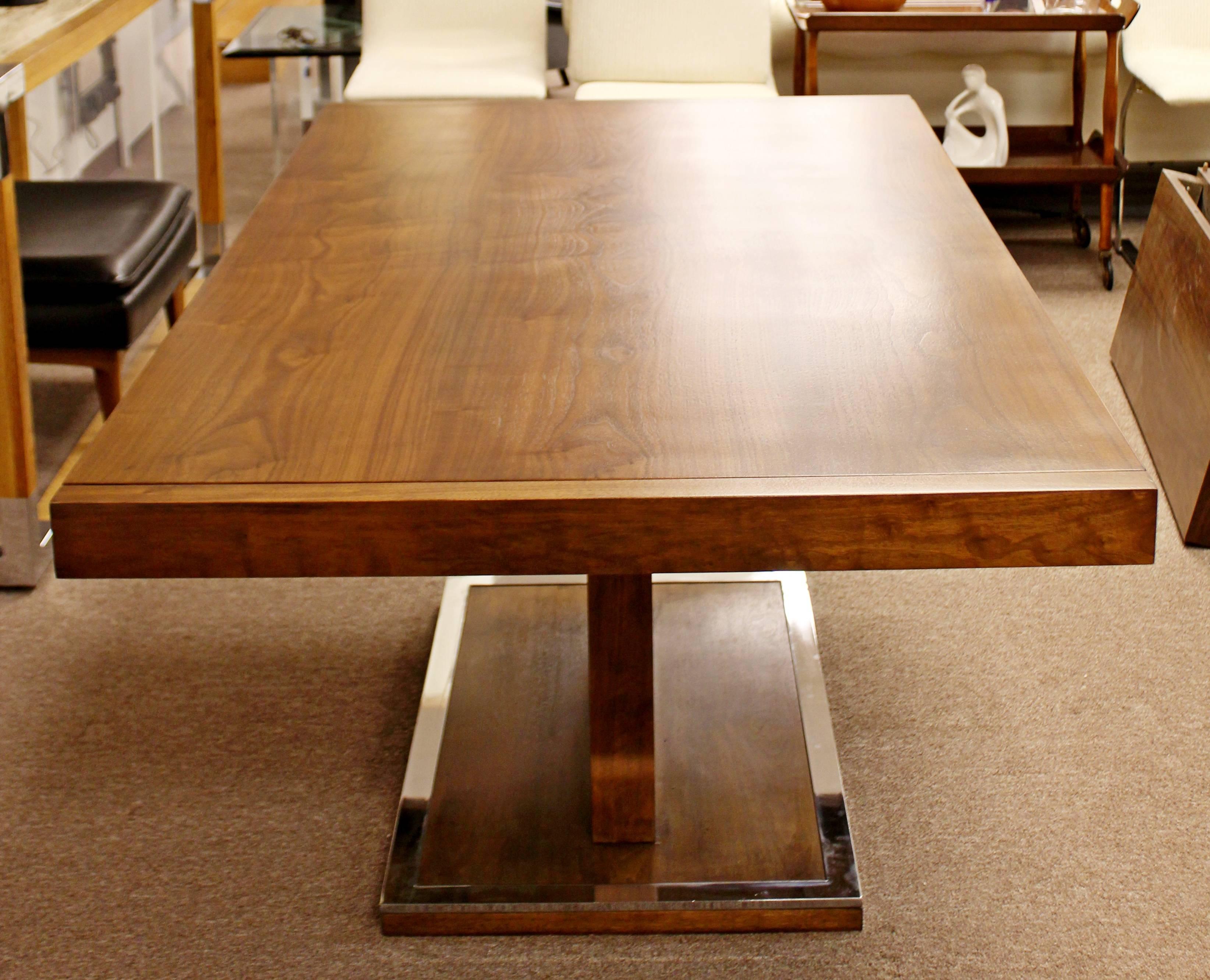 For your consideration is a fabulously unique, expandable, walnut dining table, with a chrome edged pedestal base and two leafs, by Milo Baughman for Founders Furniture Company, circa 1970s. In great condition. The dimensions are 68