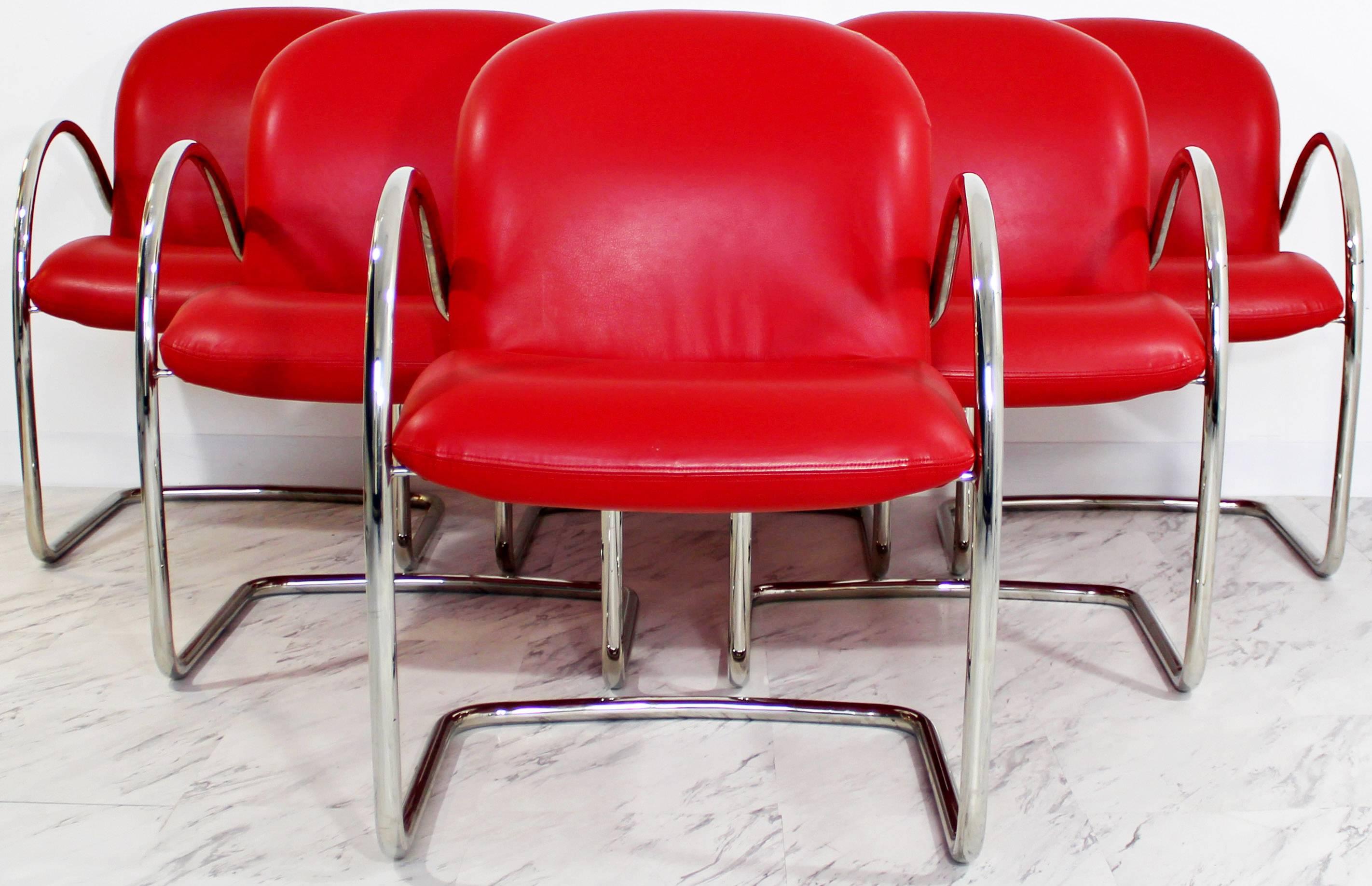 For your consideration is a brilliant set of six, red leather and chrome, dining chairs with arms by Brueton. In excellent condition. The dimensions are 22" Sq x 32" H x 18" S.H.