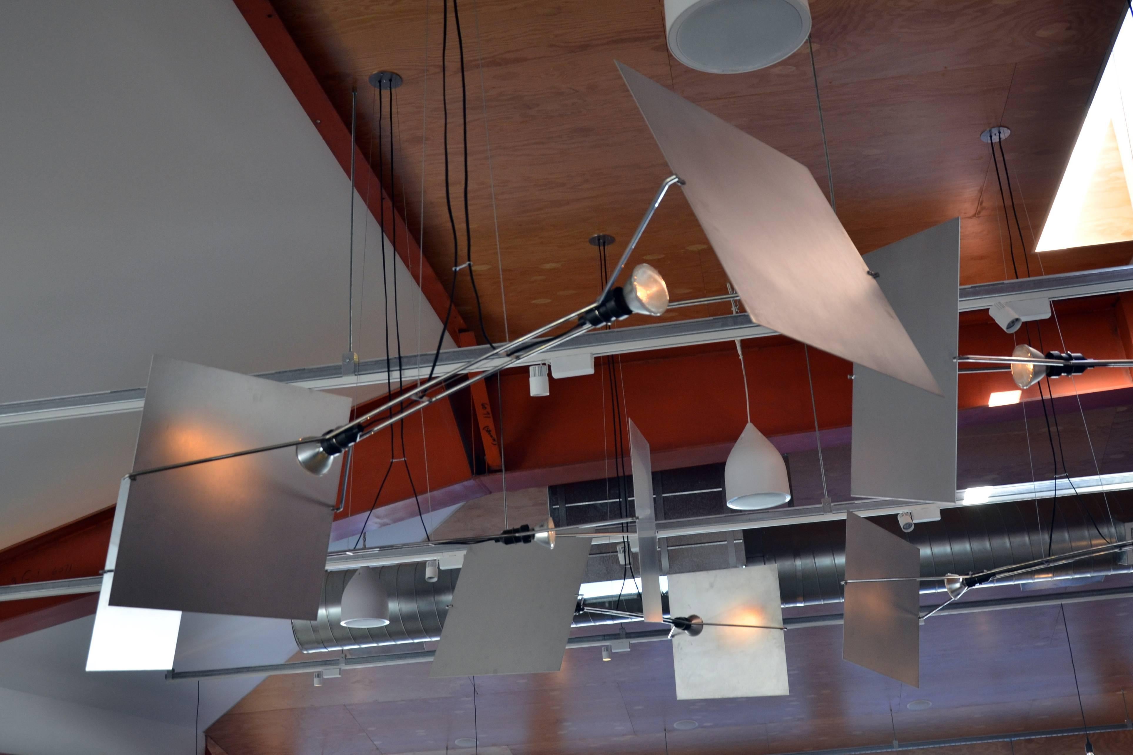 Suspended from the ceiling by wire rope, Pendas is a pared down stainless steel armature supporting two outward facing spotlights. Pivoting aluminum reflectors allow light to be directed up towards the ceiling, or down towards a table. Originally