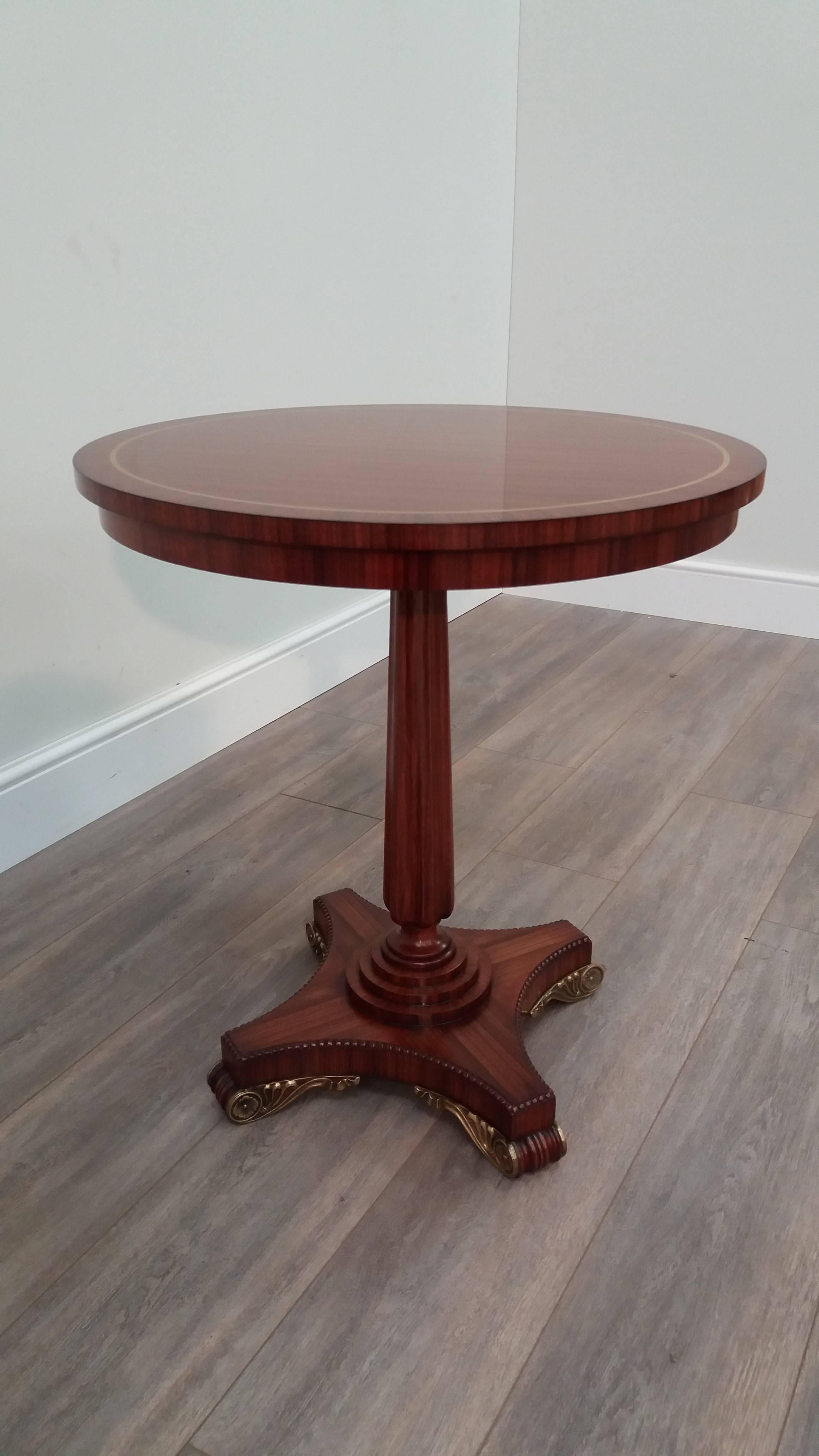 A circular occasional table with finely selected veneered top with brass inlays, above an hexagonal concave moulded column.  The four-pointed base features a beaded edge and ornate brass mounts on moulded feet.

Arthur Brett is a long-established