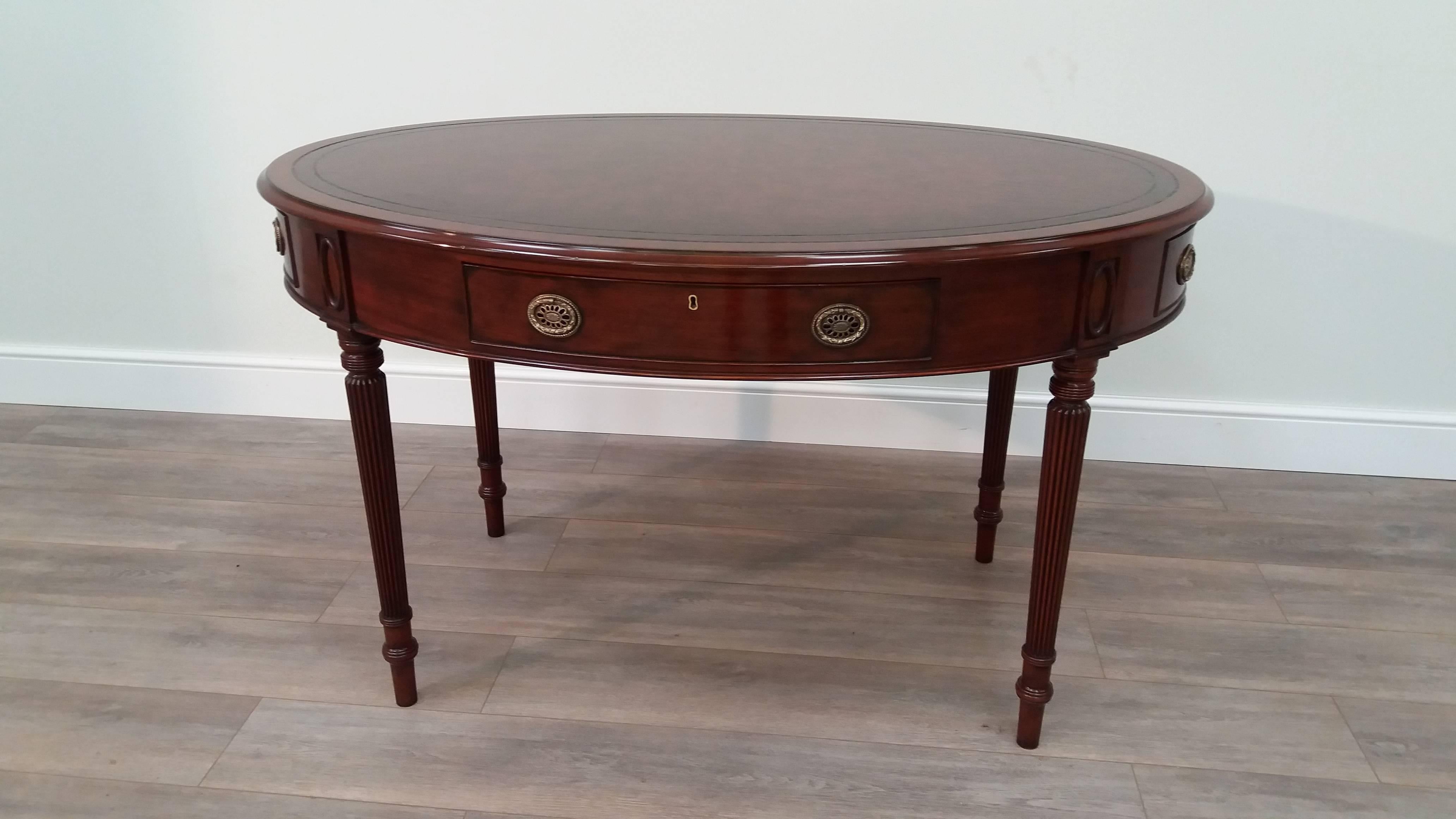 An attractive mahogany oval writing table in the Regency style on turned and reeded legs surmounted by oval patera. With one long side drawer and faux drawers at each end with brass oval plate handles. The top is lined in Arthur Brett's hand-dyed