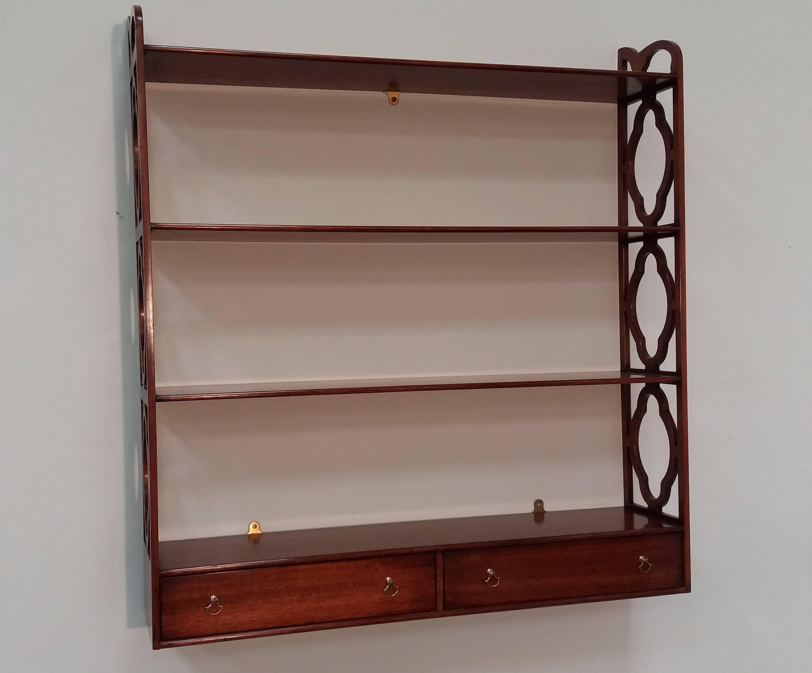 Solid mahogany wall-mounted bookshelf with hand-cut fretwork sides. Three shelves over two drawers with brass drop-pull handles.

Arthur Brett is a long-established English cabinet making business producing high quality furniture, specializing in