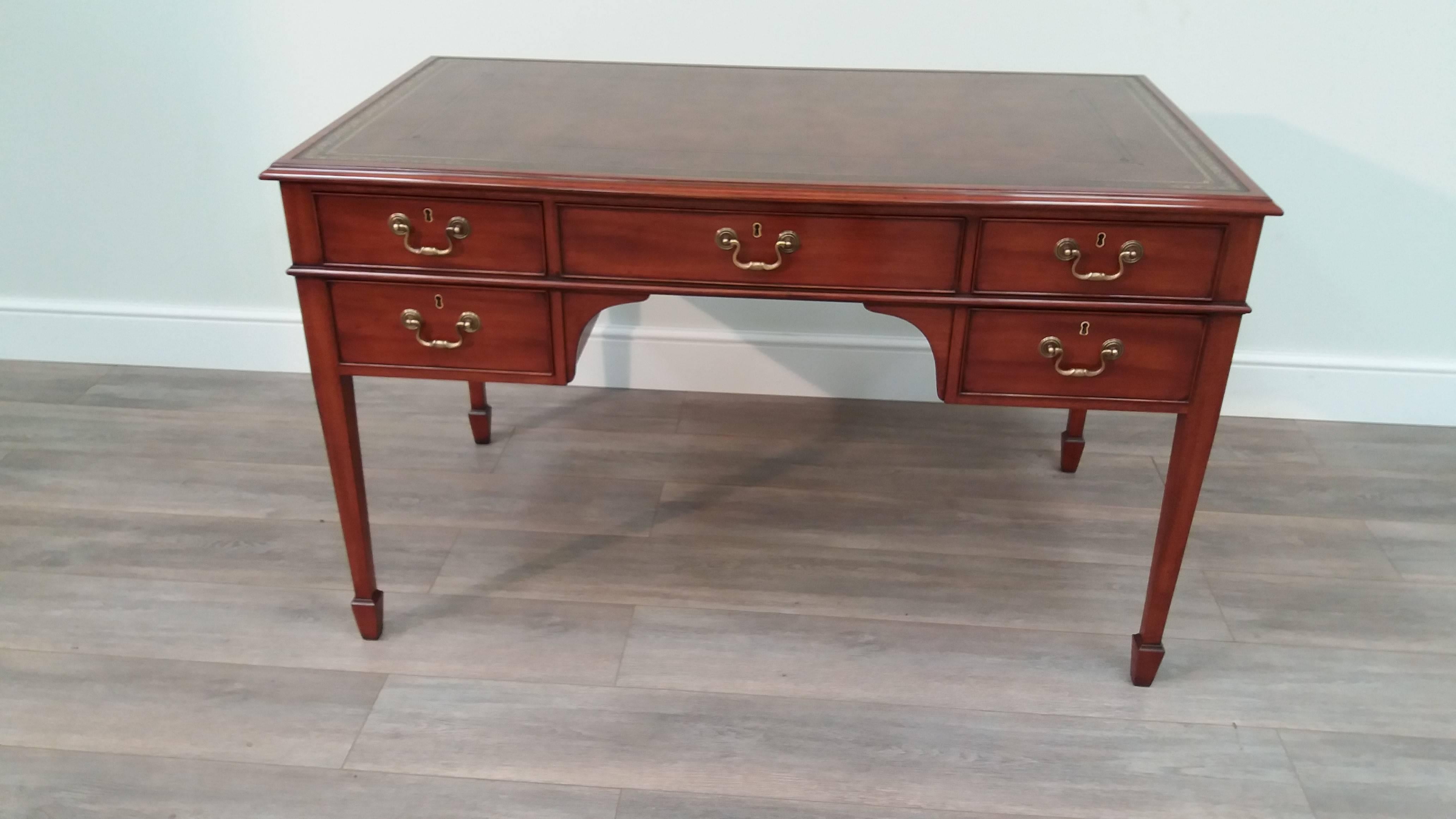 A compact Sheraton-style mahogany five drawer kneehole writing table with gilt-tooled hand dyed leather top.  the reverse side is mocked out with dummy drawers without handles.

This piece is sold with an Arthur Brett ‘X-finish’ which has been hand