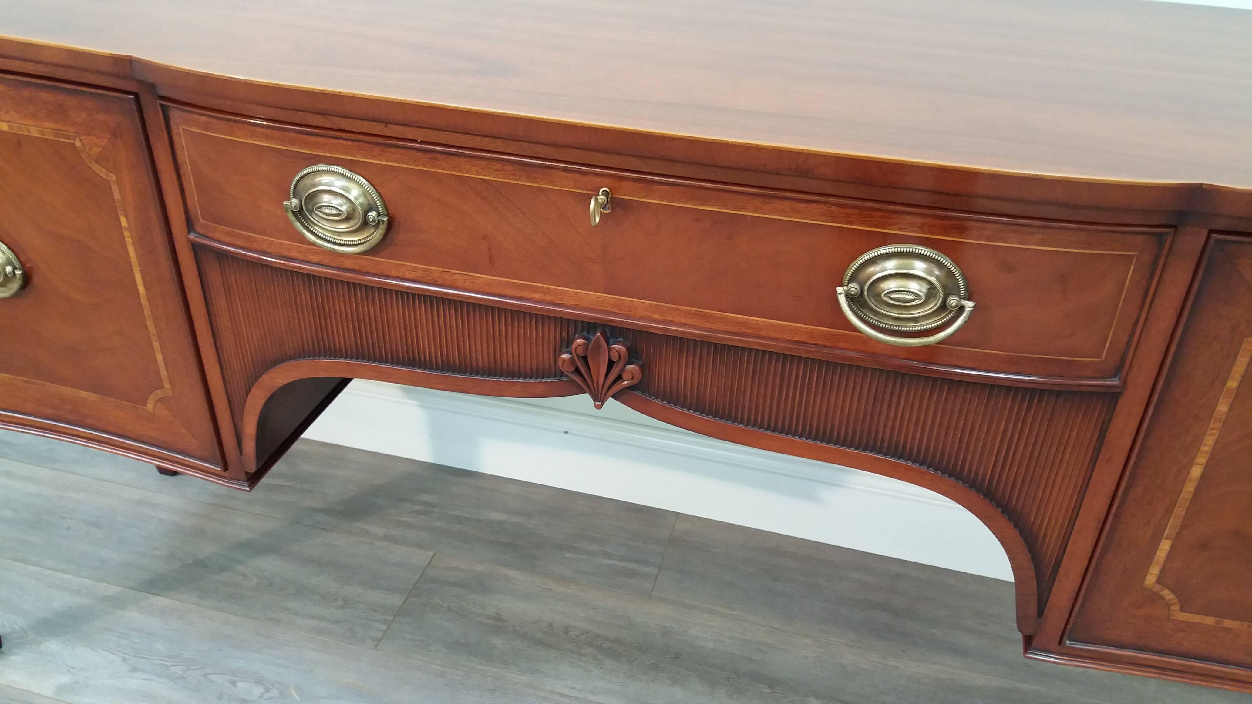 A classic Georgian serving sideboard in mahogany with a distinctive carved and fluted frieze.  Standing on tapered legs with spade feet, featuring stringing inlay and cross-banding to the top, drawer and cupboard doors and fine brass plate
