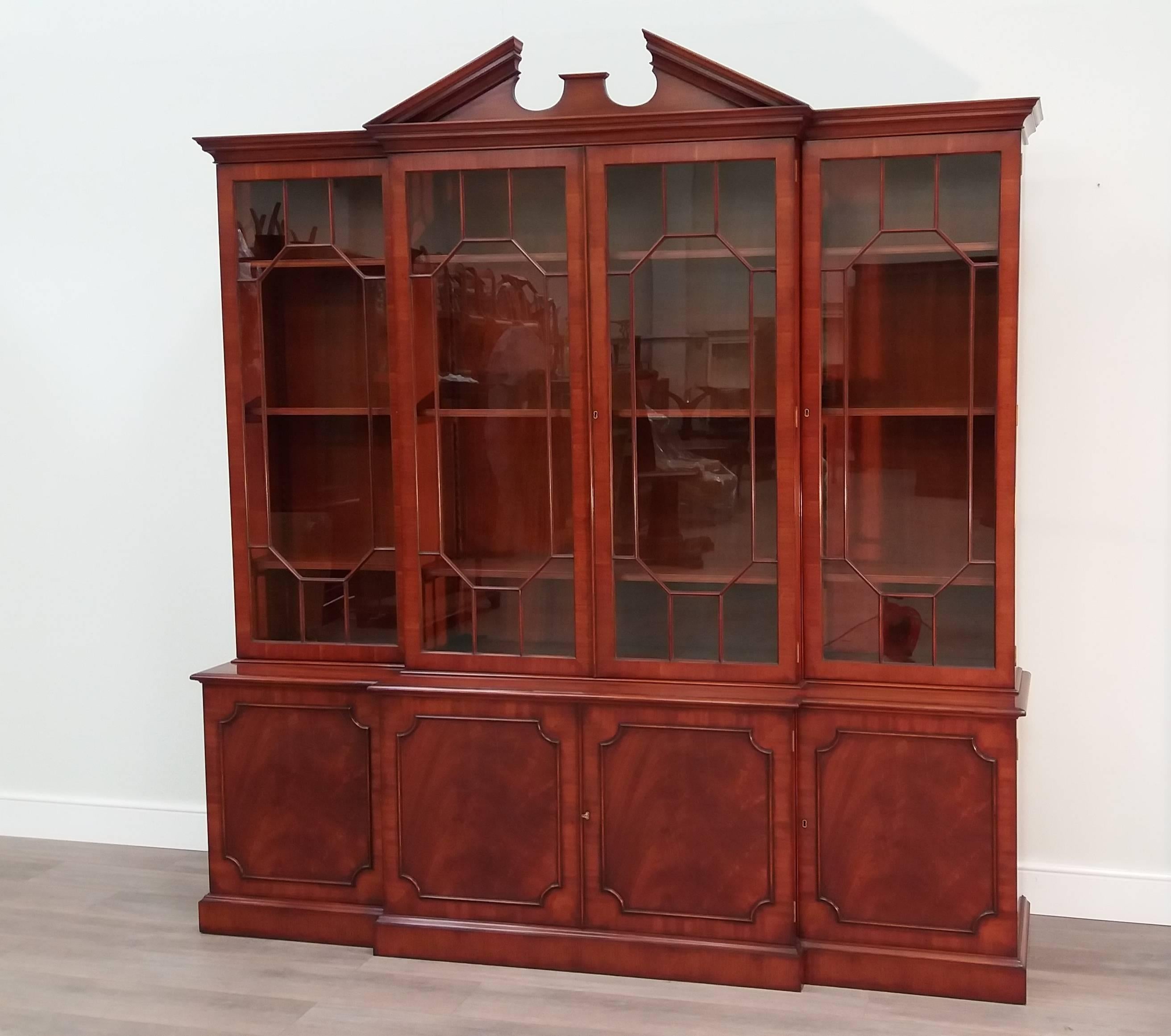 An impressive mid-Georgian style mahogany breakfront glazed bookcase, featuring a broken arch pediment and adjustable shelves behind individually glazed doors. The figured mahogany doors reveal further adjustable shelves in the base - all