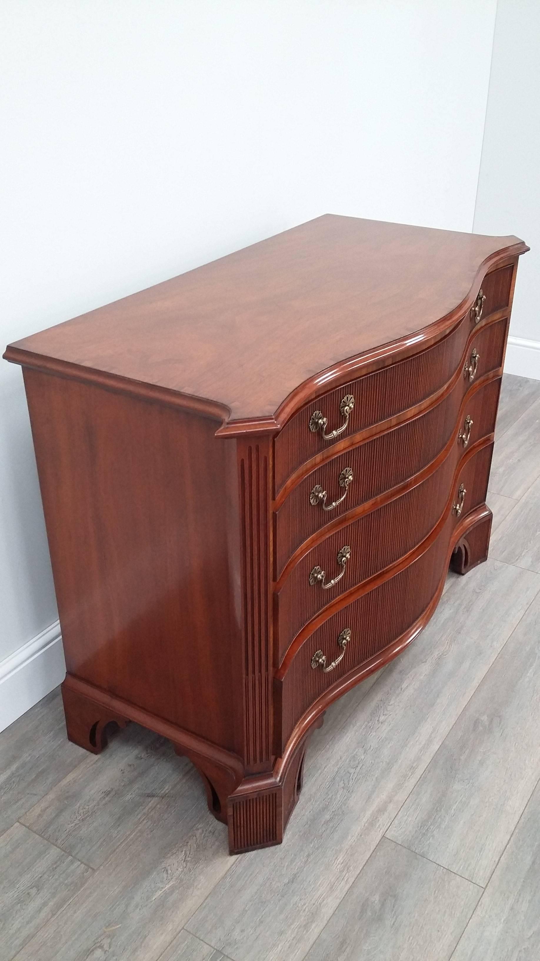 An impressive mahogany serpentine fronted chest of drawers in Chippendale style with a cross banded top and canted and fluted corners.  Reeded mouldings cover the four drawer fronts and the pierced carved feet.  With brass bail pull handles on