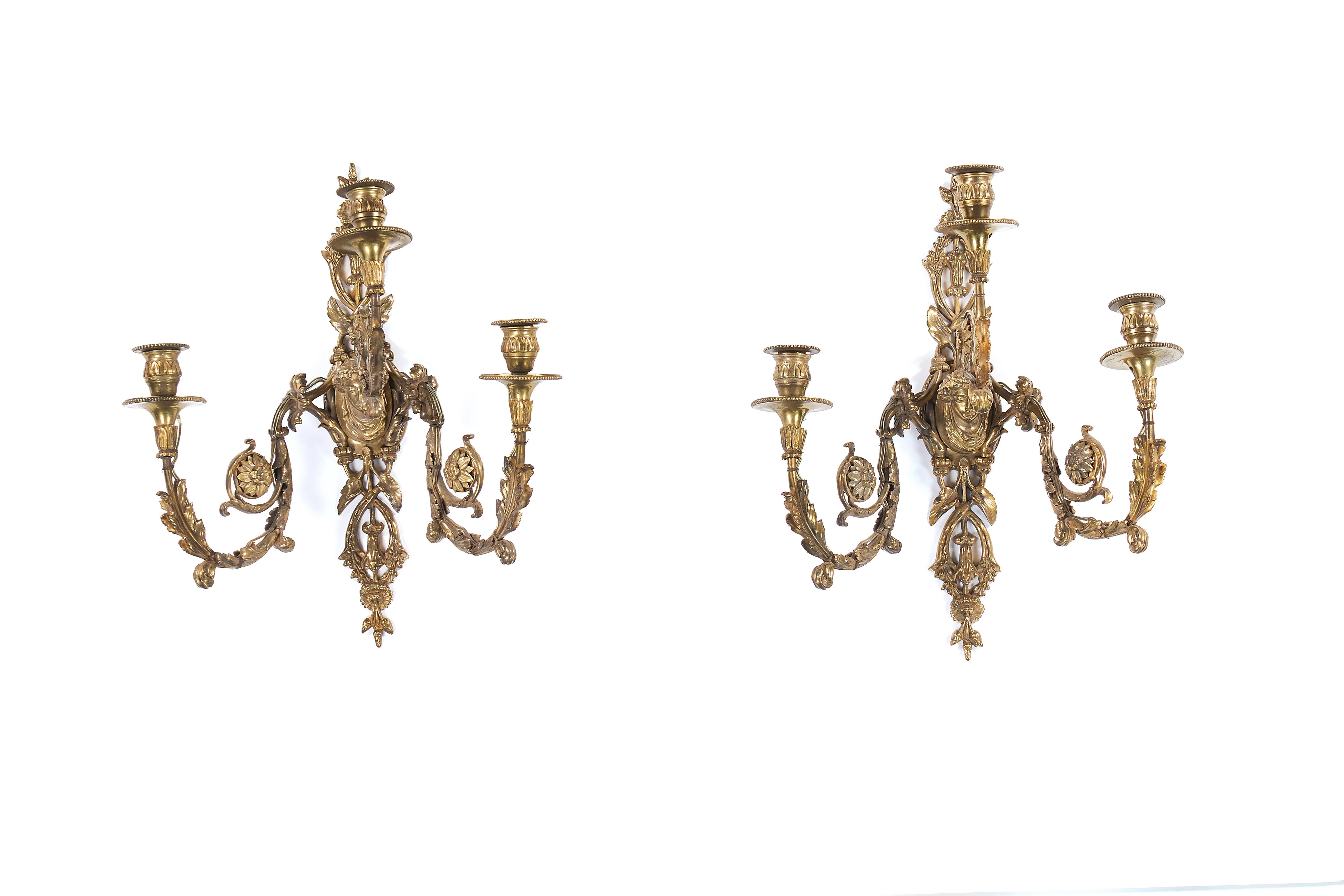 A pair of late 19th century gilt bronze three-light wall appliqués
in the manner of Edward F. Caldwell and Co., New York
The foliate back-plates centred by a female bust issuing three scrolling branches, terminating in circular drip-pans and