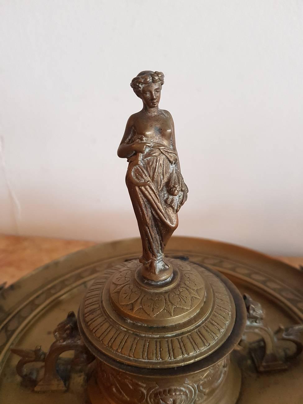 Late 19th century bronze inkwell holder with various decorations including a lady on the lid, the ears in an Art Nouveau shape with leaves and on both sides of the inkwell animal heads. The glass jar has some chips.

The measurements are,
Depth