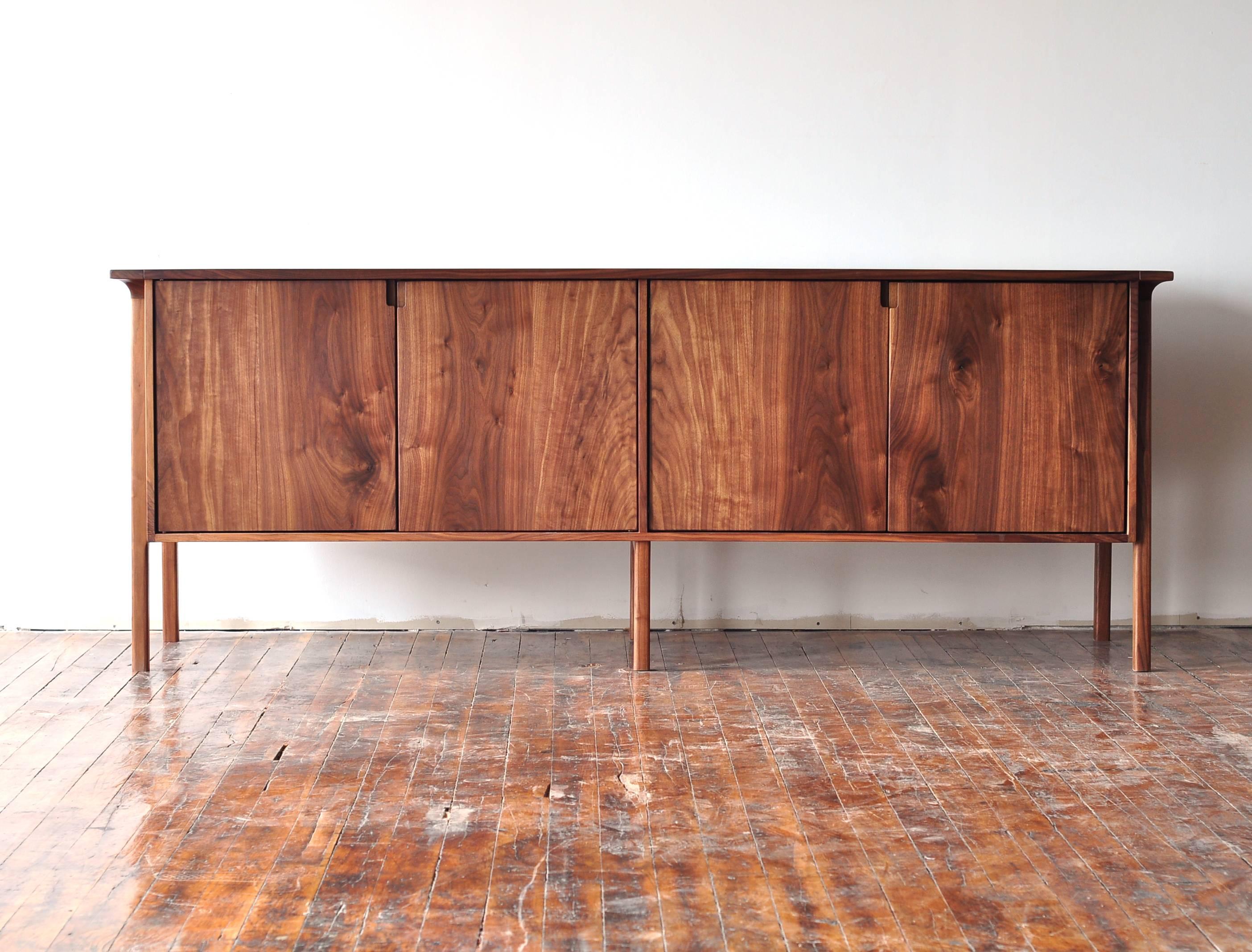 The ST01 is a long storage piece of solid walnut and could be used as a sideboard, credenza, or media cabinet. It features outer legs that extend up the sides of the case and are sculpted into the overhanging top. The simple solid wood doors and