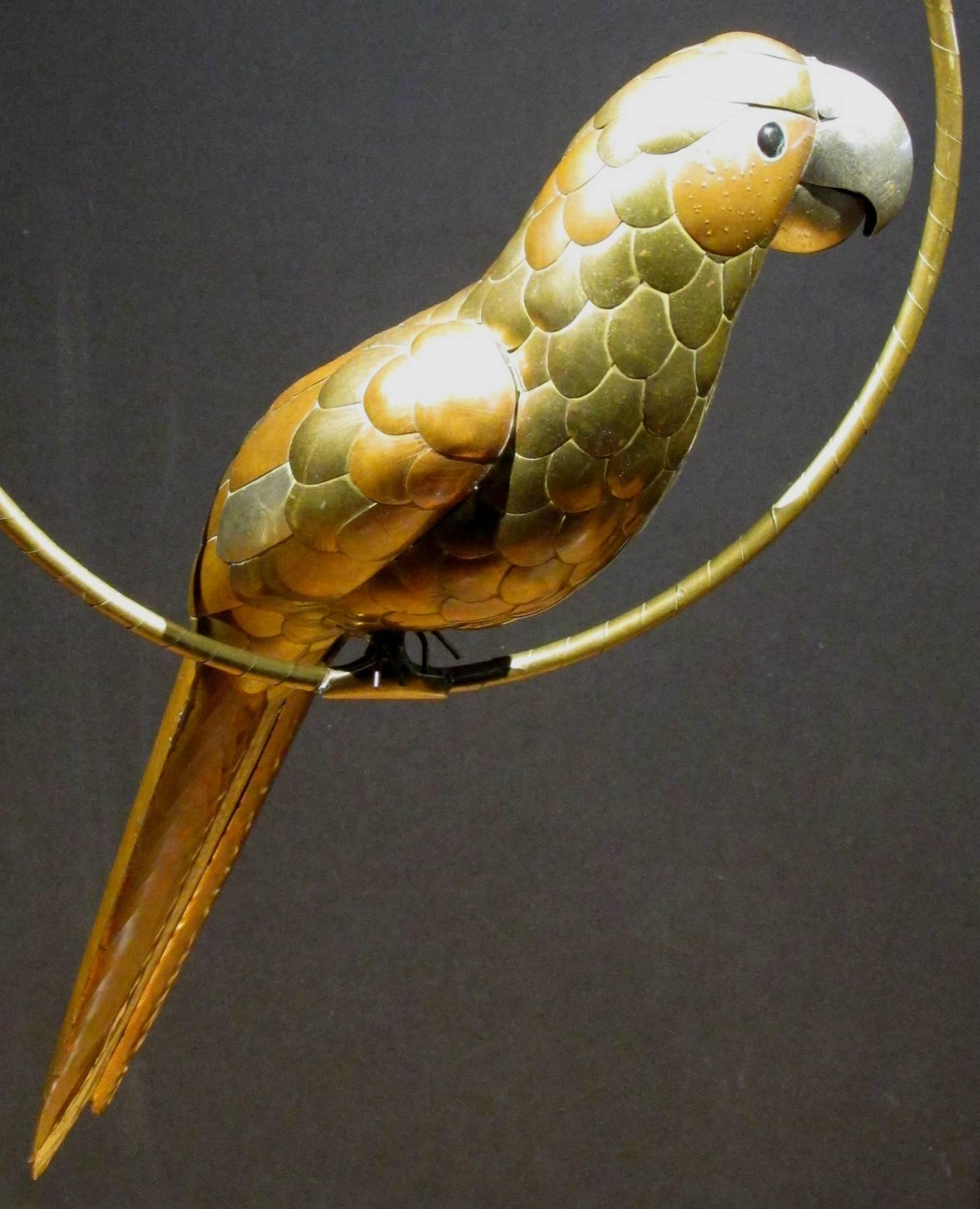 A whimsical Mid-Century Modern figure of a hanging brass and copper parrot, having a silvered beak and glass eyes, perched within its original circular copper hoop.
Measures: Length of parrot is 17", the hoop diameter is 11"