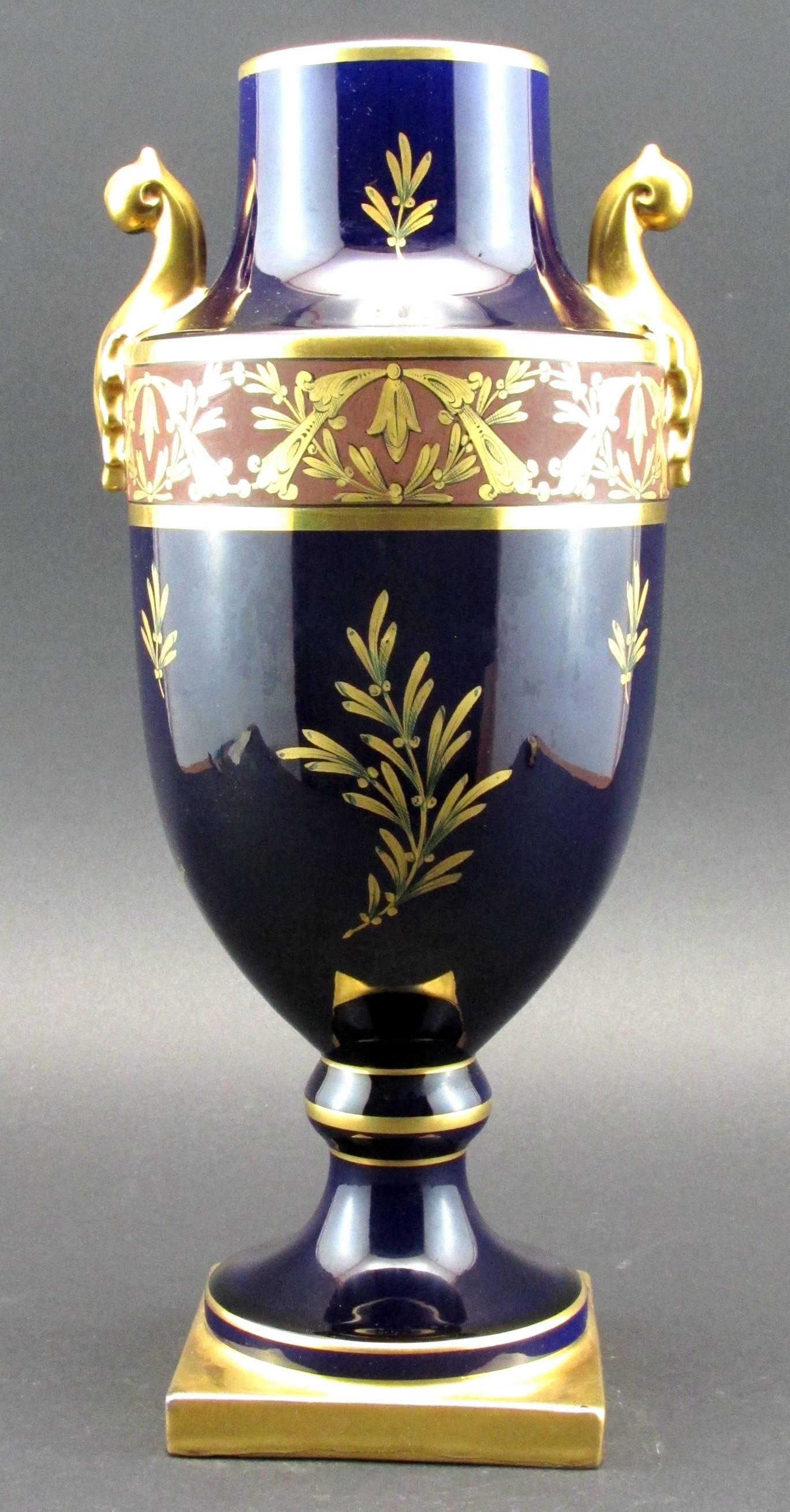 The exceptionally large cobalt glazed urn-shaped body richly decorated with cornucopia & foliate gilt motifs, sided by stylized palmette-shaped gilt handles. Signed on the body in gilt script ‘Pinon Heuze’, the underside of the base bearing