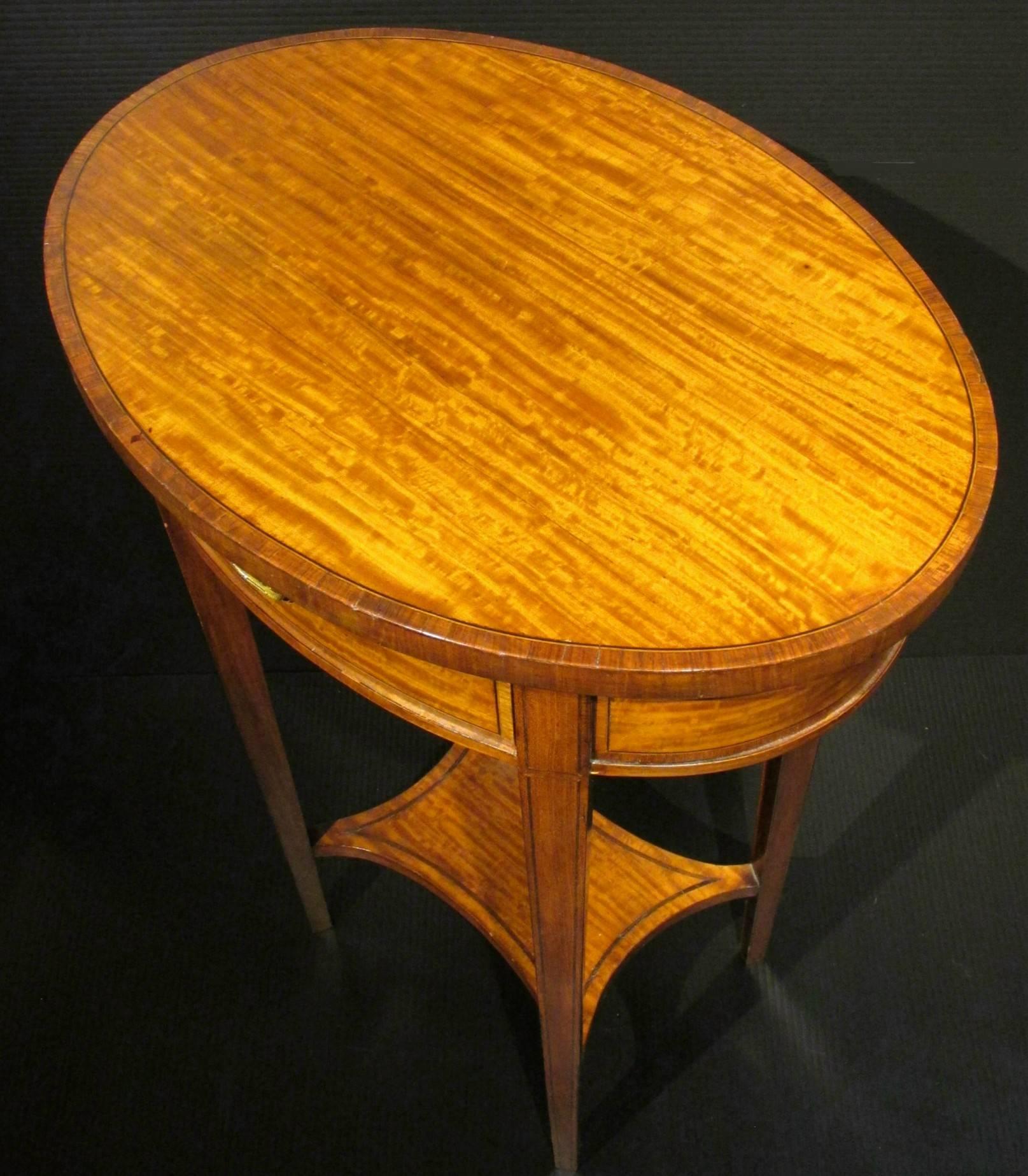 A very elegant satinwood occasional table showing a richly figured oval top accented with kingwood crossbanding and ebony stringing, surmounting a conforming frieze fitted with a flush mounted drawer, raised overall upon four squared and tapering