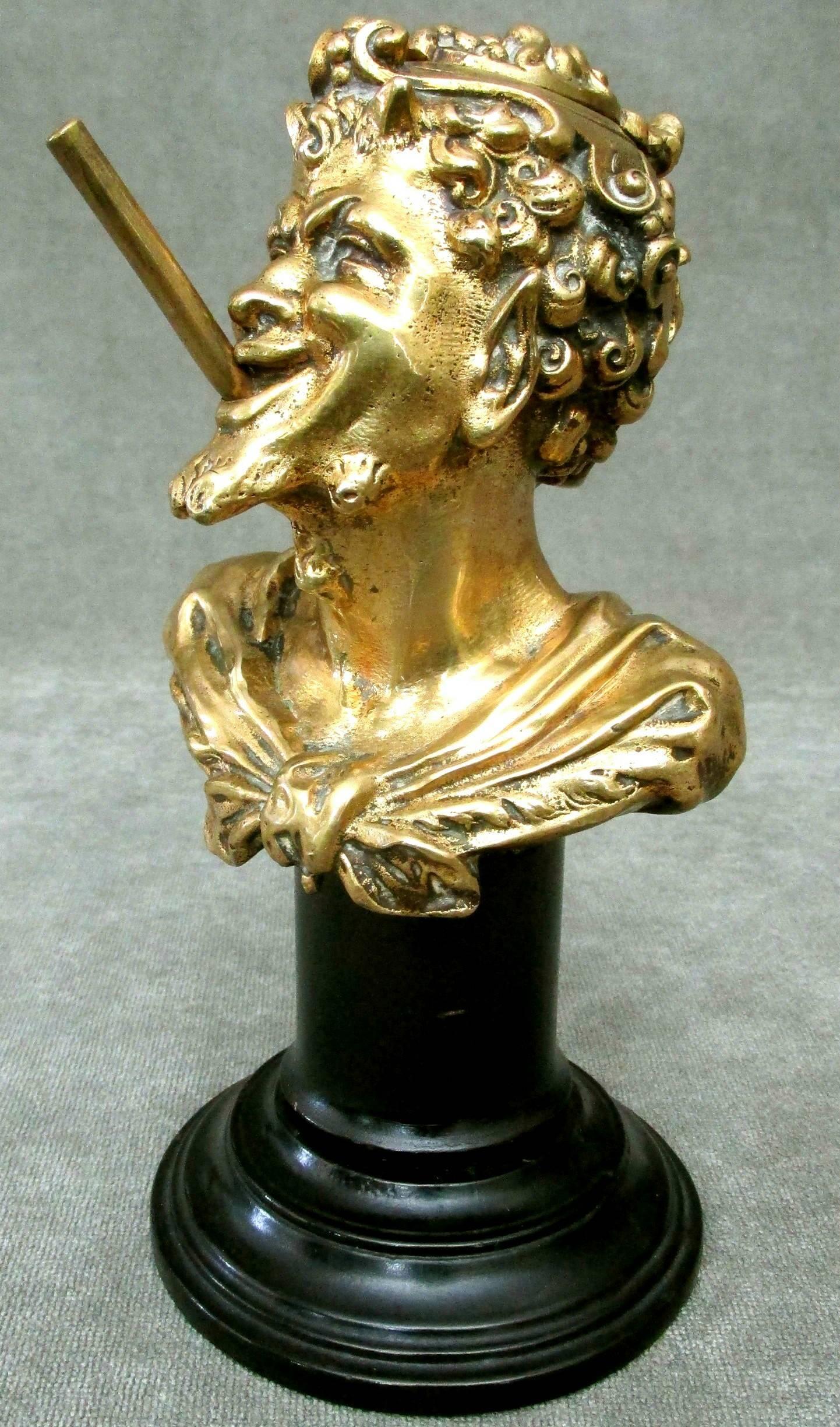 The finely cast and chiseled features of a gilt bronze satyr clenching a ‘cigar’ shaped wick holder in his mouth, the head fitted with a hinged skullcap opening to a reservoir. Raised upon a turned and ebonized wooden column.

International clients
