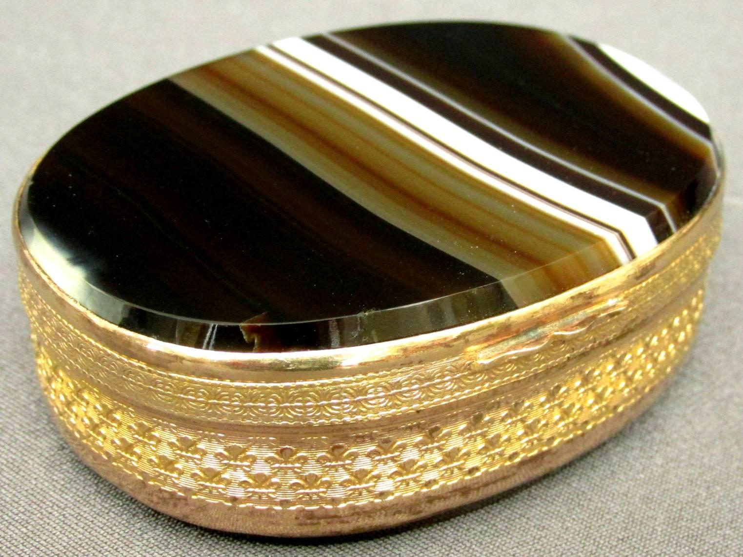 The large and hinged gilt metal oval body having a running band of embossed thistle motifs, encasing two conforming agate panels with graduated white and brown striations.

