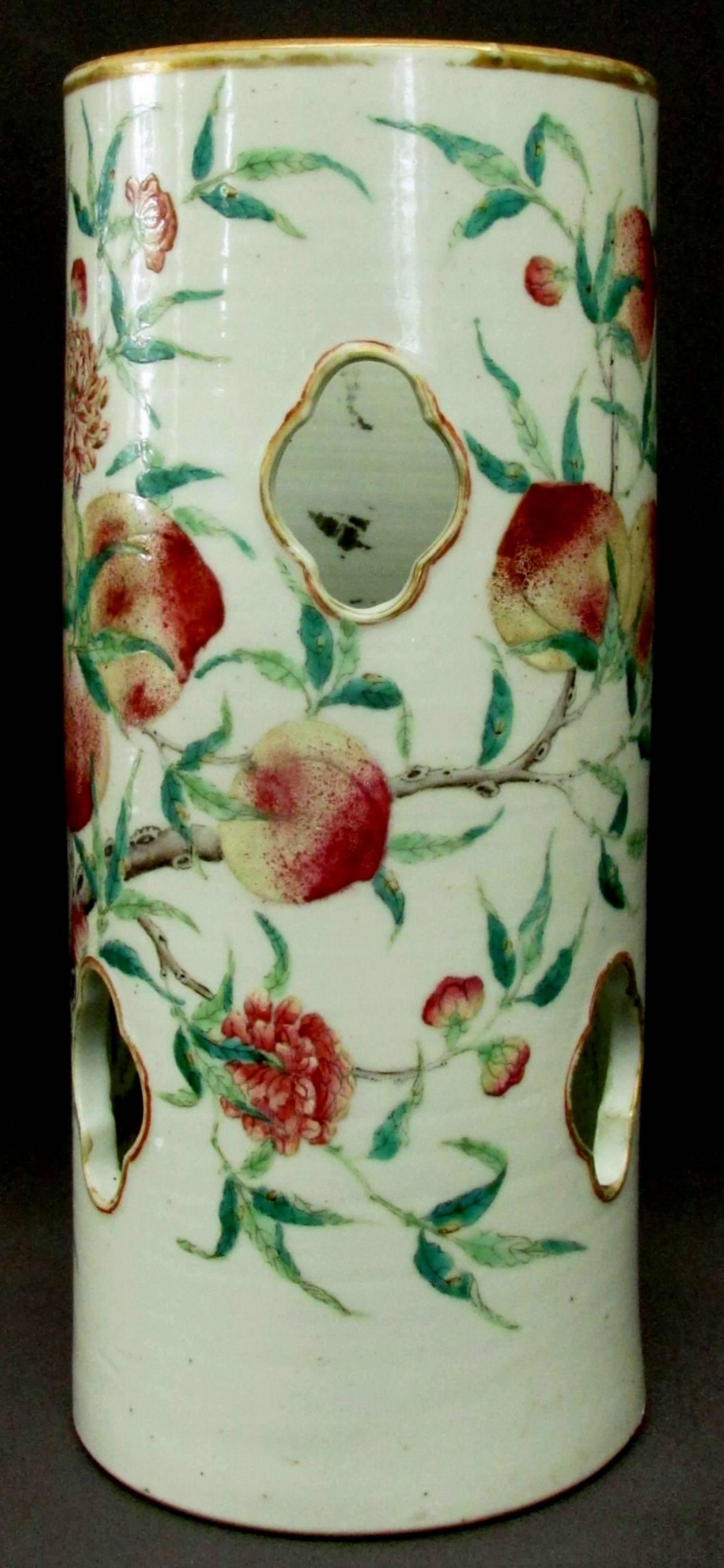 The pierced cylindrical body decorated with enamels showing leafy branches with peach clusters and fruit blossoms. Iron red seal script mark and wax export approval seal on underside, remnants of an old paper label affixed to rim.

International