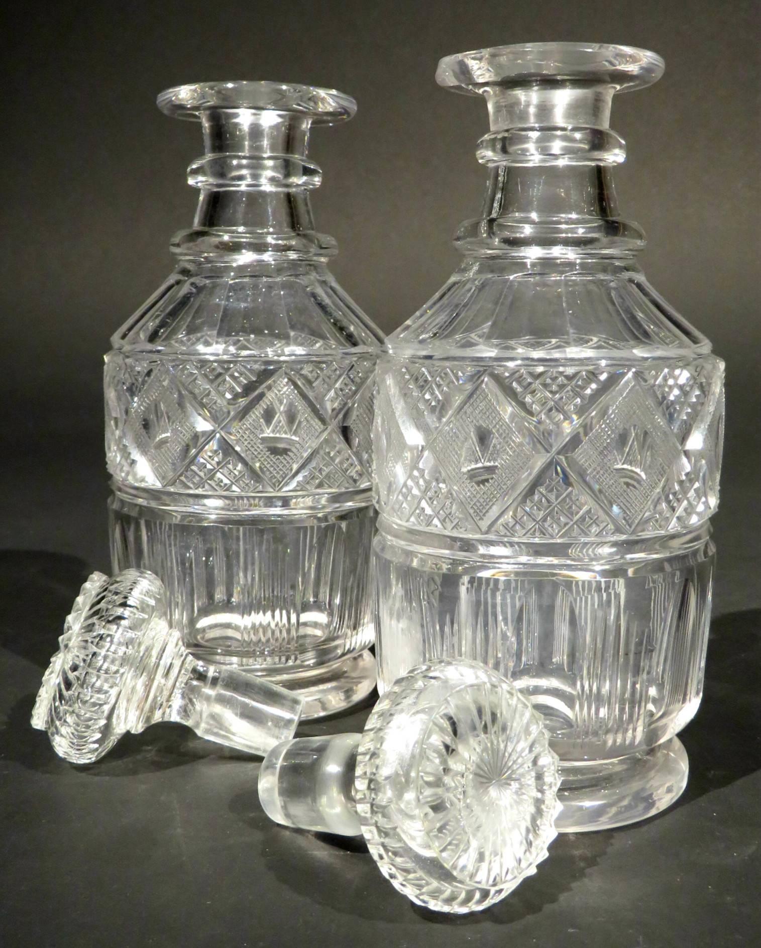 A fine pair of early 19th century cut-glass pint spirit decanters showing straight sided bodies with faceted, fluted & diamond cut detail, rising to double ringed necks with flaring rims fitted with their original dedicated stoppers, the undersides