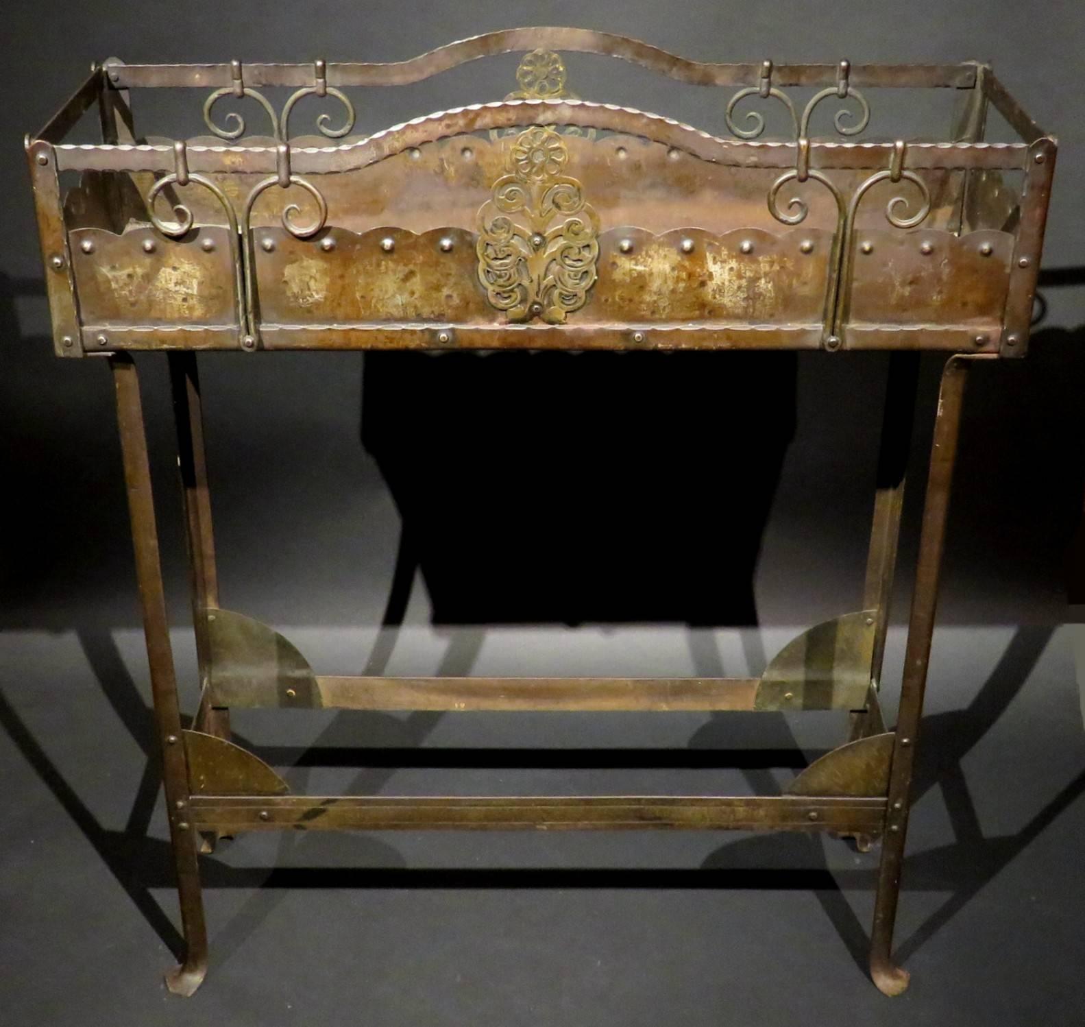 The riveted framework showing a sheet-iron body with an undulating gallery, decorated with hand-hammered organic and whiplash elements, raised overall atop four angular supports braced by flattened stretchers with gilt-patinated spandrels. In