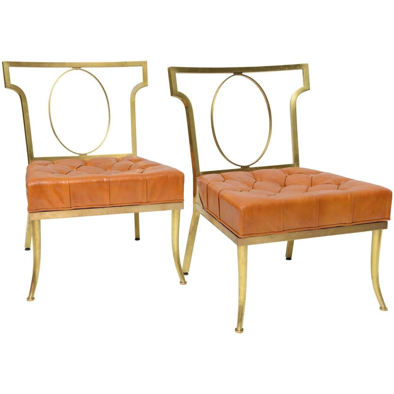 Pair of solid brass slipper chairs are Haines' interpretation of the ancient Greek 'klismos.' He created three versions of the chair: this sleek open-back design with a brass oval filling the negative space. They retain the original orange leather
