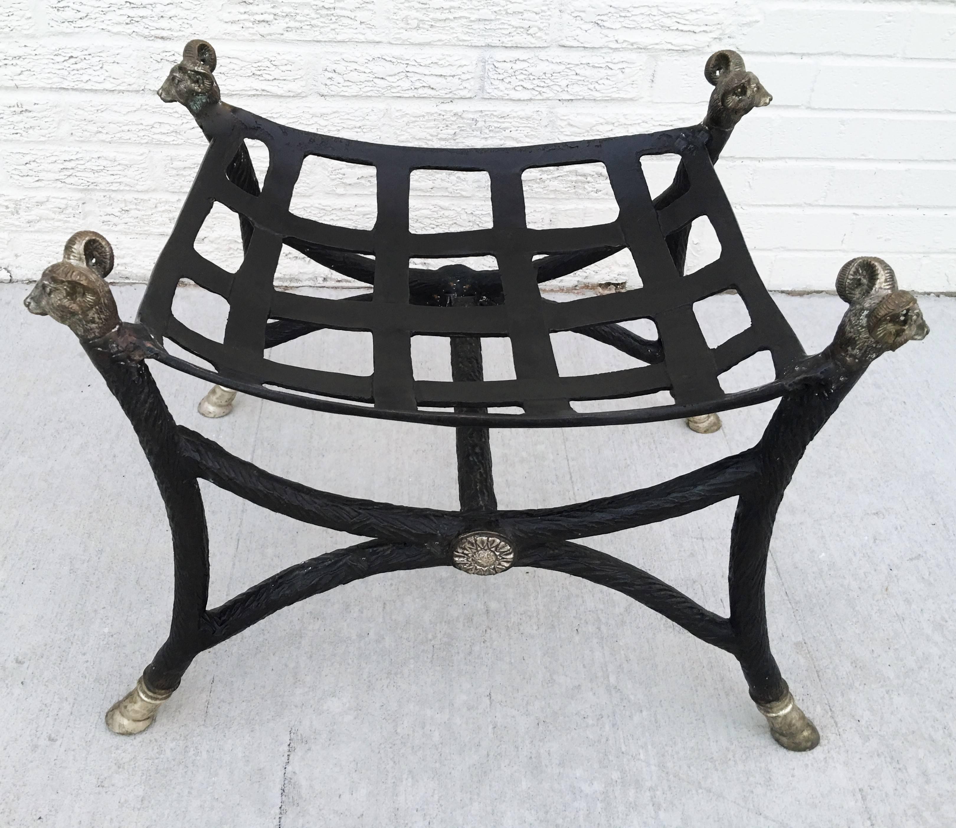 Hand-Forged bench in Curule form, removable silk cushion, X-Frame with hoof feet, ram-heads with undulating-manes and each grasping a crescent moon- shaped ring. The distinctive heavy weight and hammered surface of the iron are both integral