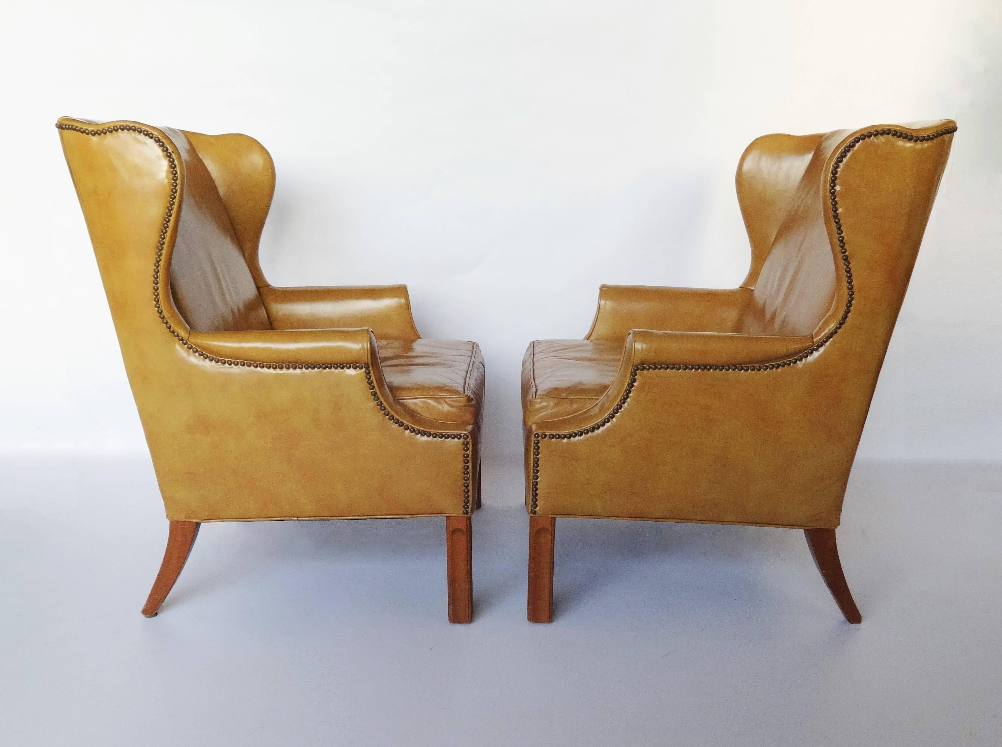 A good George III style pair of light tan leather wing armchairs. With a winged back, rolled arms, close nailed brass studded detail. Raised on square supports united by a H-stretcher. Can be used as is or re-upholstered to liking. Inquire about our