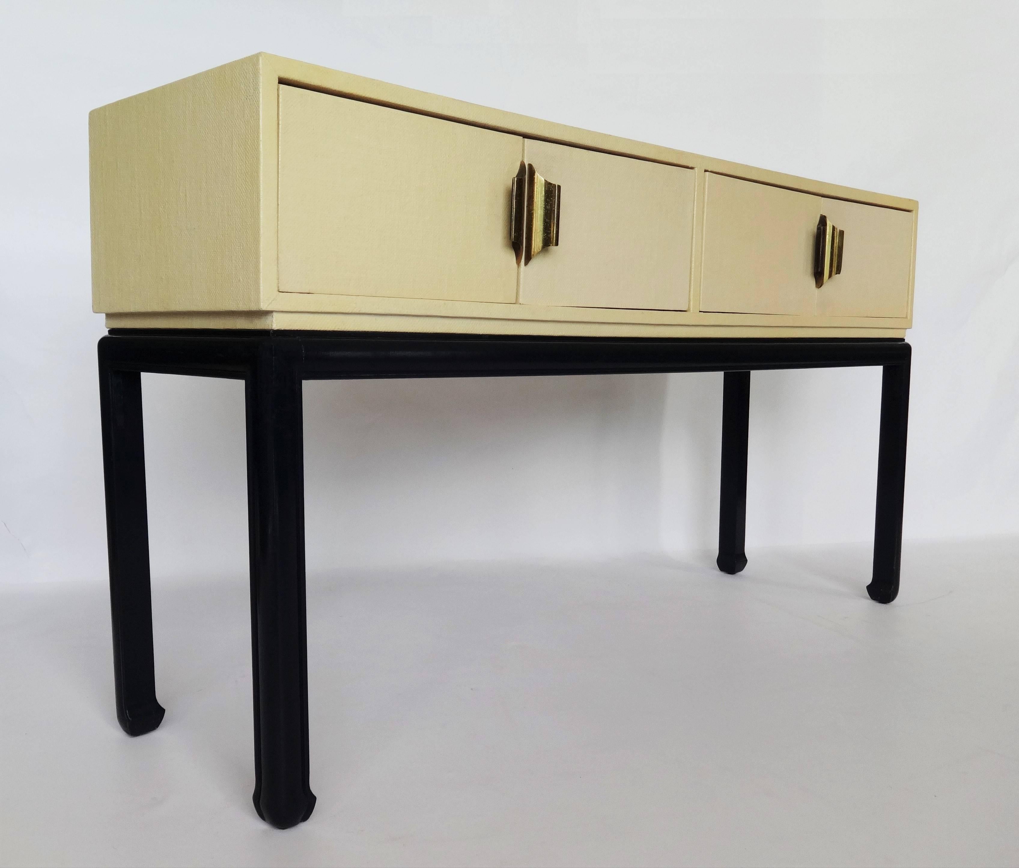 A modern vintage grasscloth wrapped console or buffet with four doors. Asian inspired brass hardware and ebonized base, in the Chinese Chippendale style. Very practical and extremely good looking.