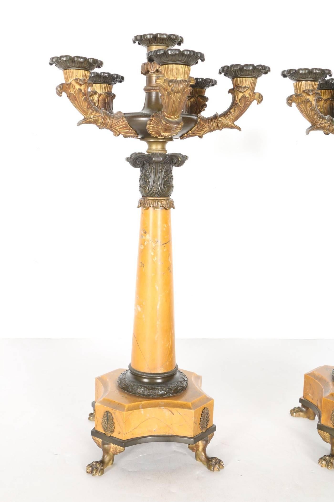 A pair of Charles X or Louis Philippe period patinated bronze and sienna marble featuring six candle holders, scalloped and floral accents, the columnar standards supported on gilt metal animal paw feet.
 