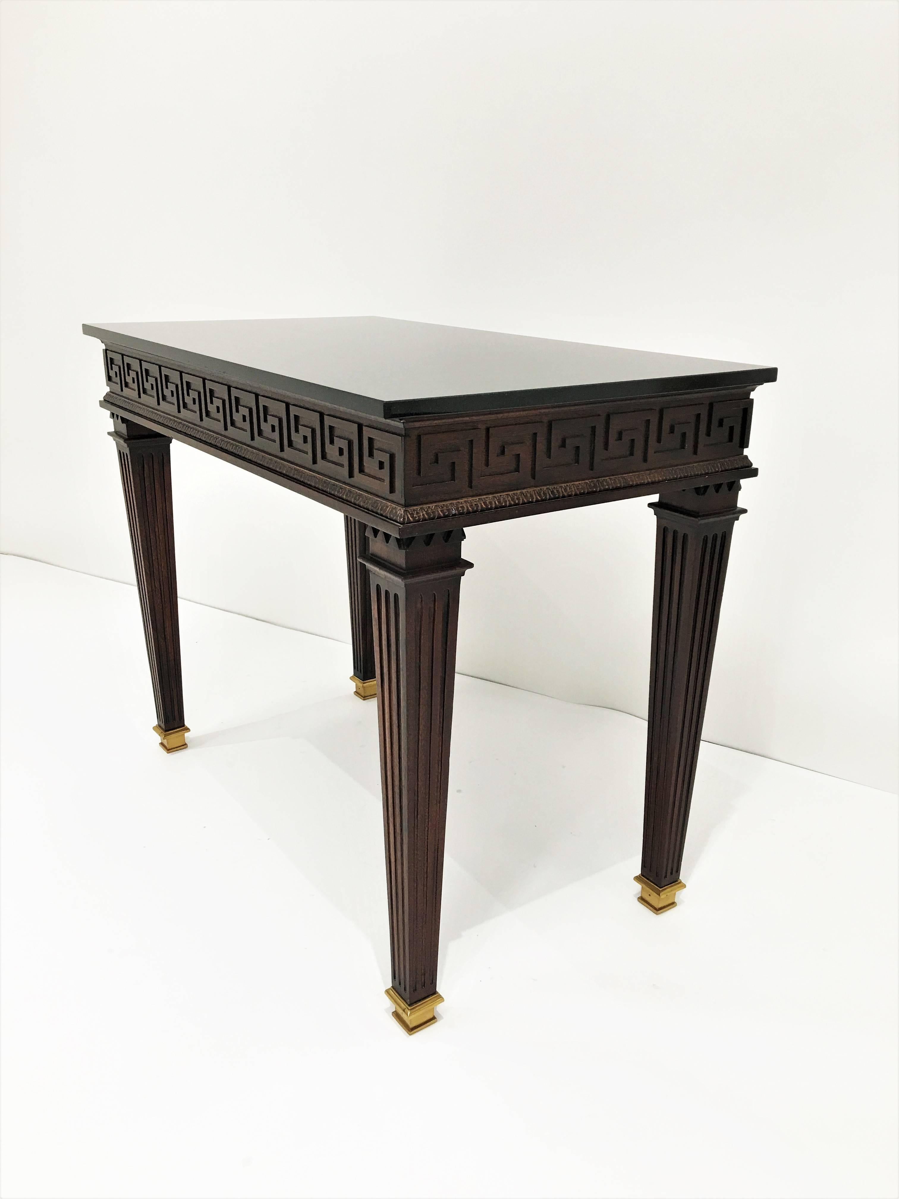 Neoclassical, circa 1920s. Elegant console table with newer black granite top over a narrow frieze decorated with brass Greek key pattern, supported by four fluted legs ending in brass caps.