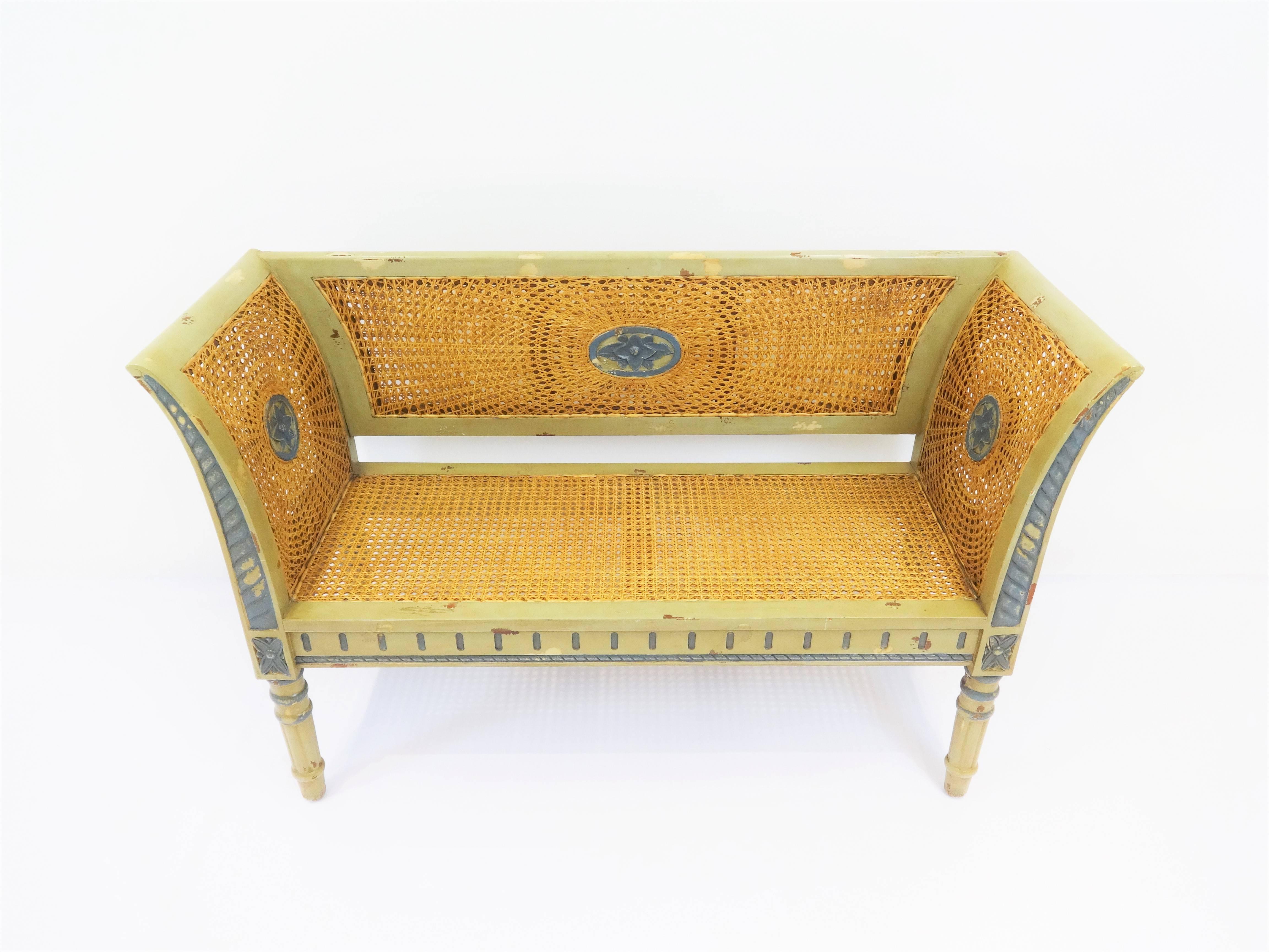 A wonderful vintage Regency style cane settee/bench highlighting beautiful intricate handwoven cane on back, arms and seat with hand-carved accents and turn spindle legs. Great distressed look.